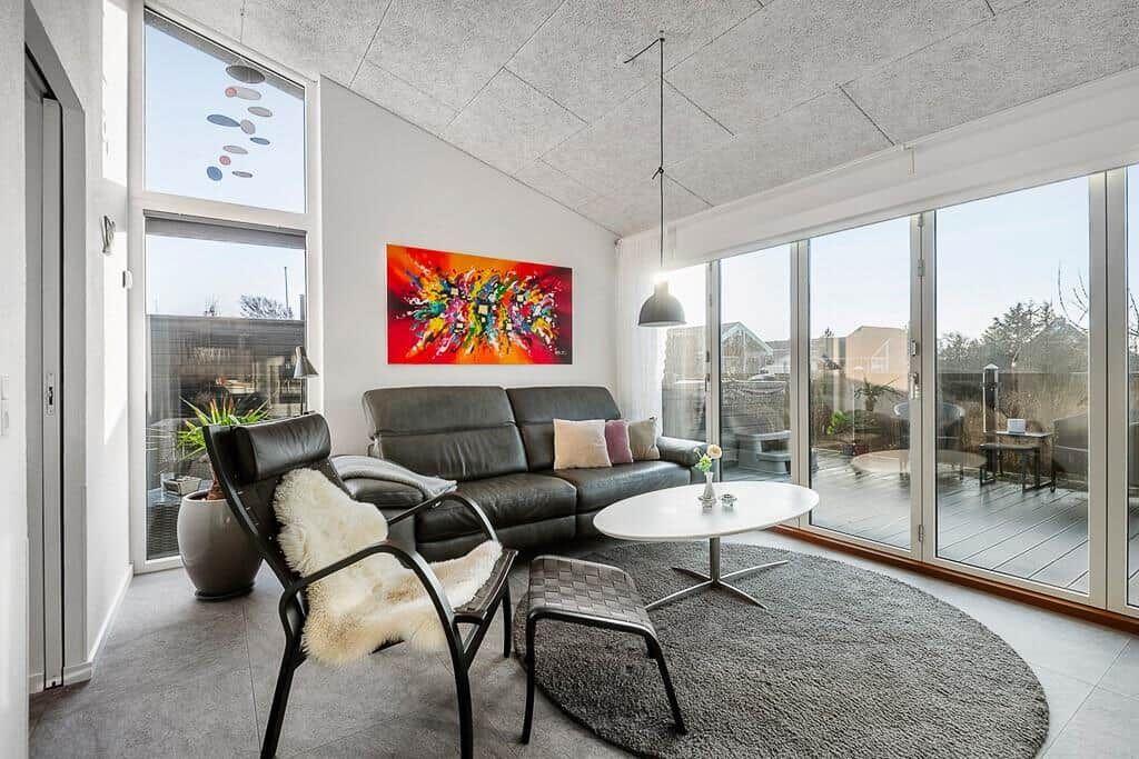 Wohnzimmer mit Ledersofa, Sessel und runden Teppich. Große Fenster und Glasschiebetüren.