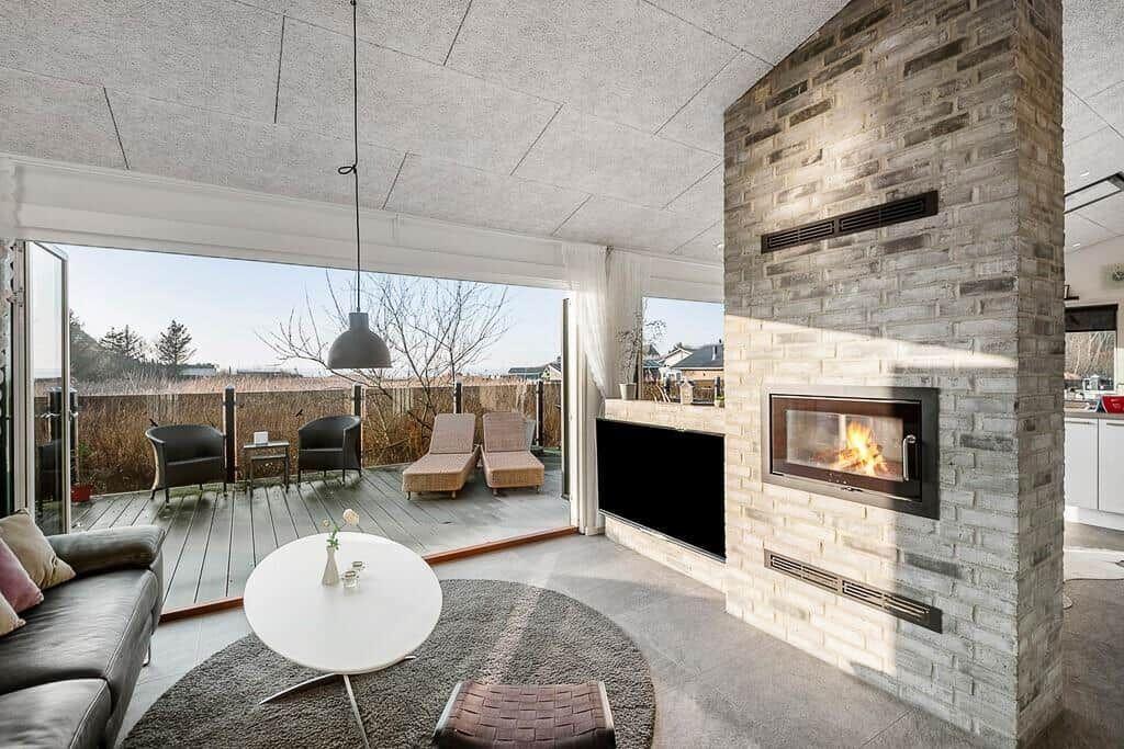 Wohnraum mit Kamin, Terrasse und Sitzgelegenheiten. Moderne Einrichtung und großzügige Fenster.