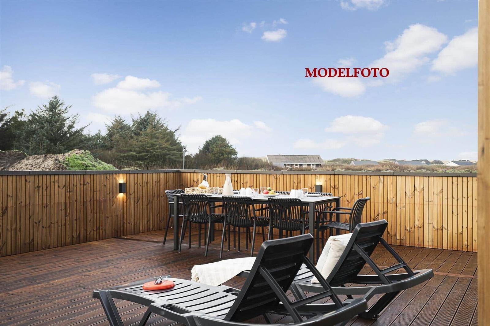 Terrasse mit Tisch, Stühlen und Liegestühlen. Holzgeländer und Blick auf Grünflächen.