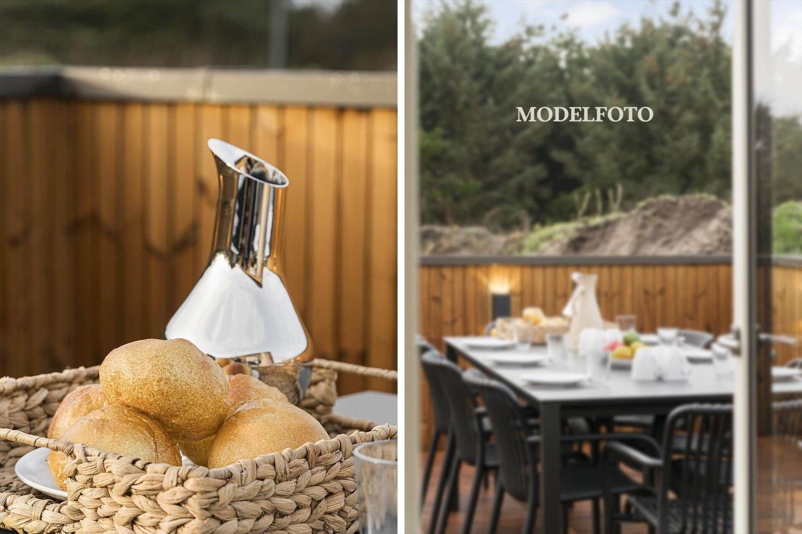 Außenbereich mit Tisch, Stühlen und Brotkorb. Hintergrund: Holzgeländer und Wald.