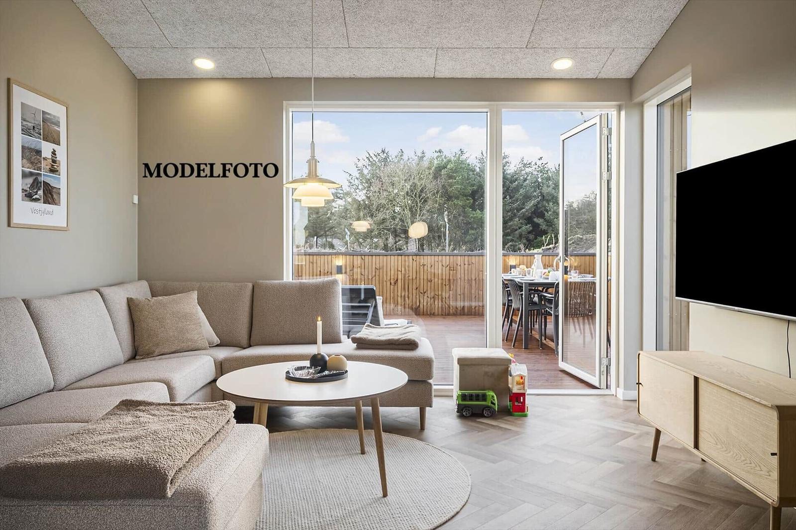 Wohnzimmer mit Sofa, runden Tisch und TV. Durchgehende Glasfront zur Terrasse.
