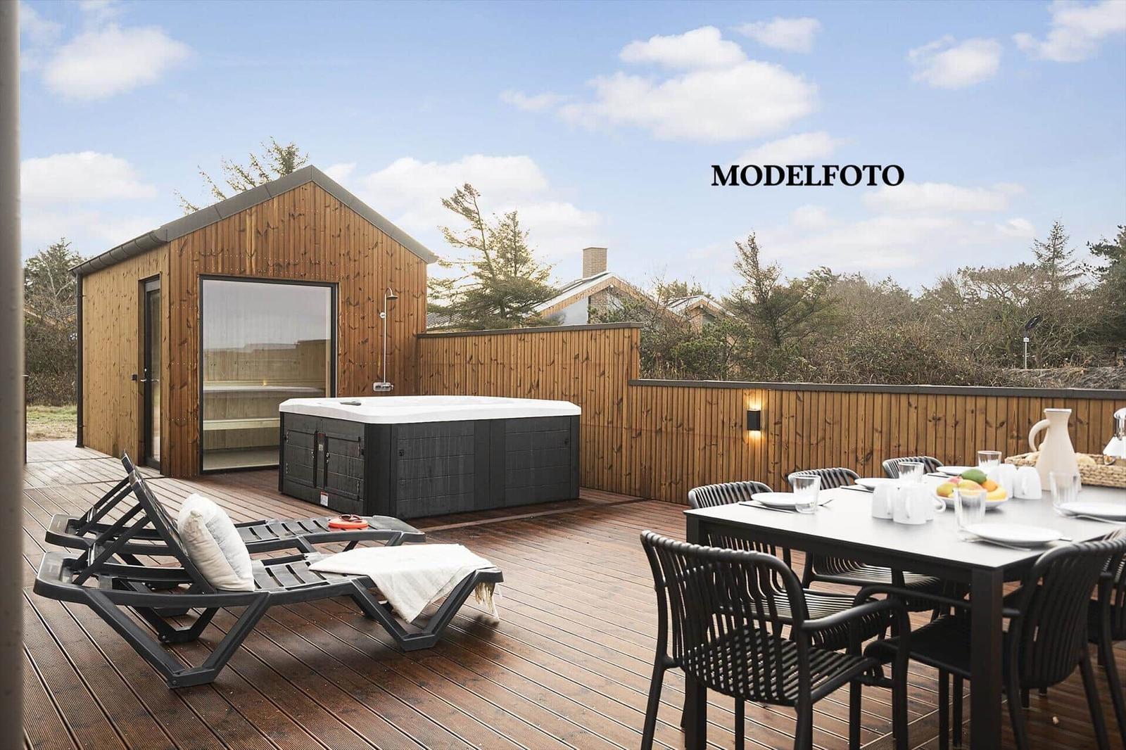 Terrasse mit Liegen, Whirlpool und Essplatz. Hintergrund: Holzhaus und Bäume.