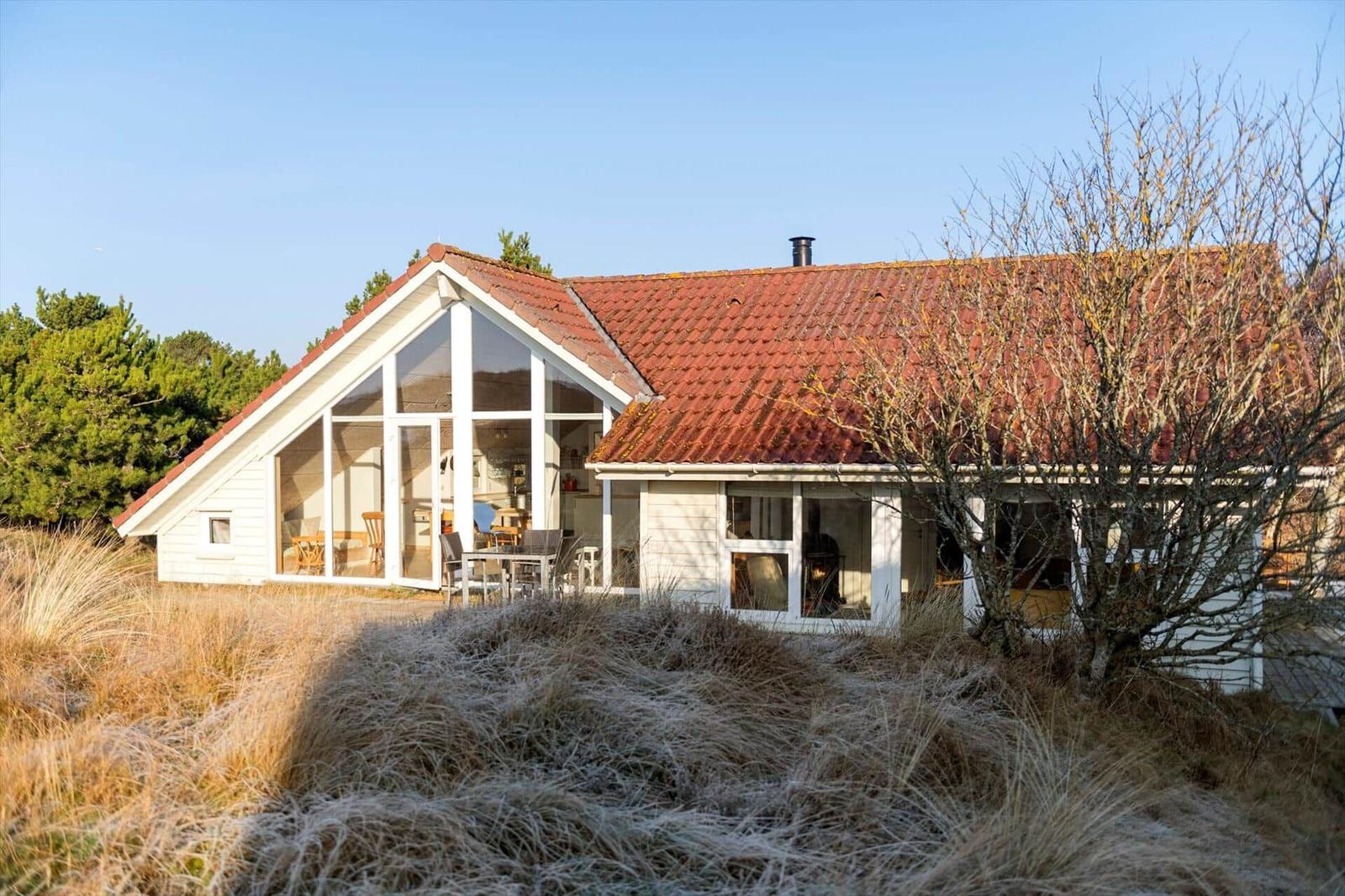 Ein weißes Haus mit rotem Dach und großem Fensterbereich steht in einer grasbewachsenen Landschaft.