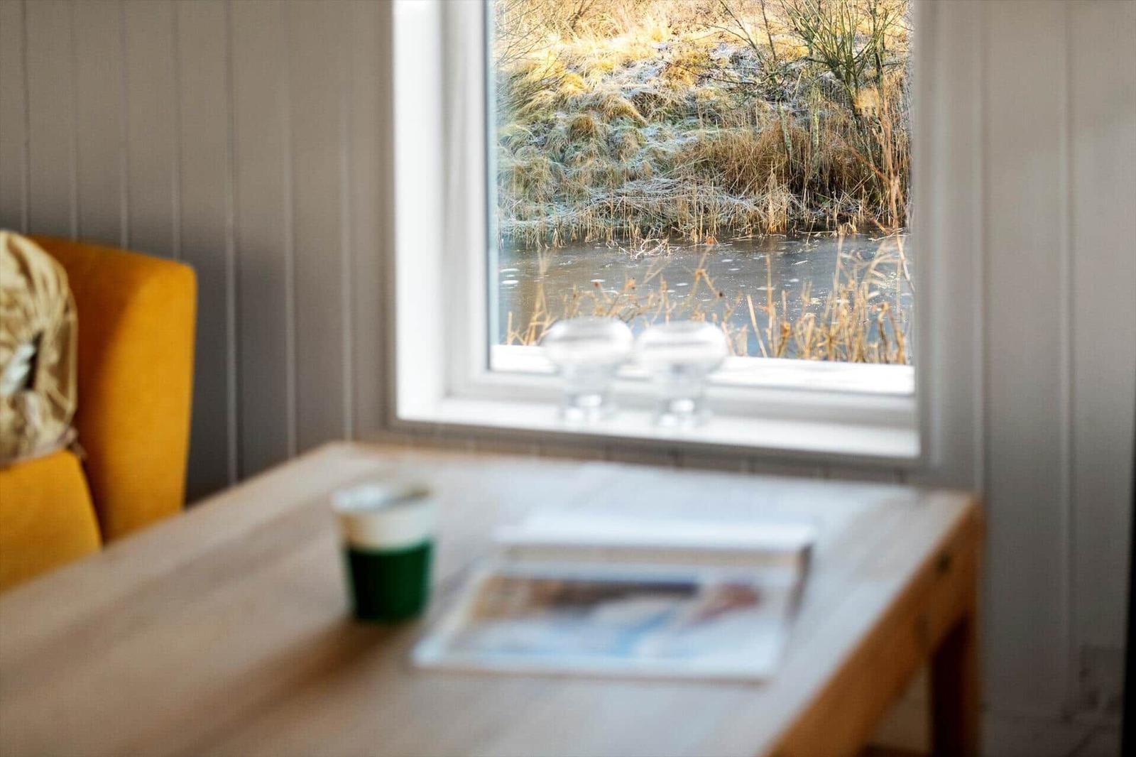 Ein Tisch mit Tasse und Zeitschrift vor einem Fenster mit Blick auf einen gefrorenen See.