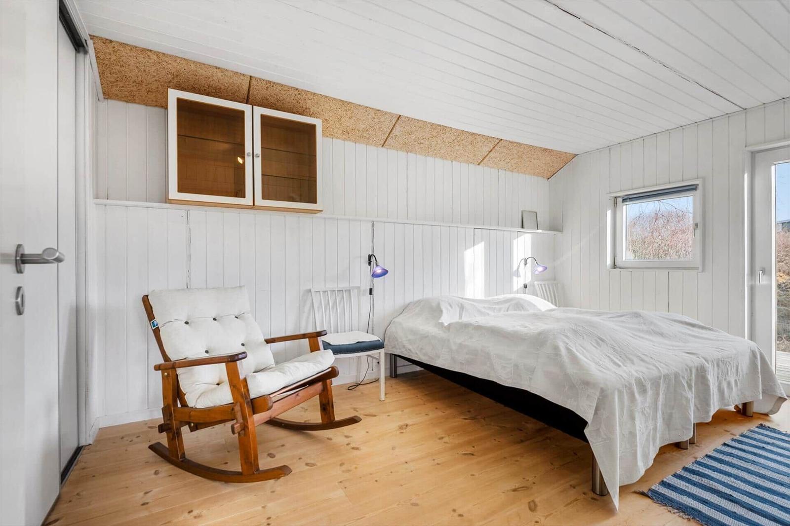 Schlafzimmer mit Bett, Schaukelstuhl und Holzboden. Weiße Wände und Decke.
