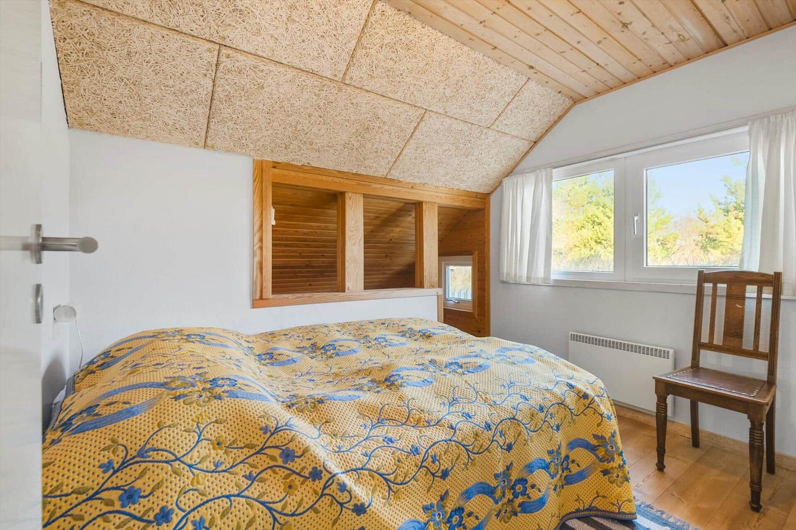 Schlafzimmer mit Bett, Holzdecke und Fenster mit Blick auf Bäume.