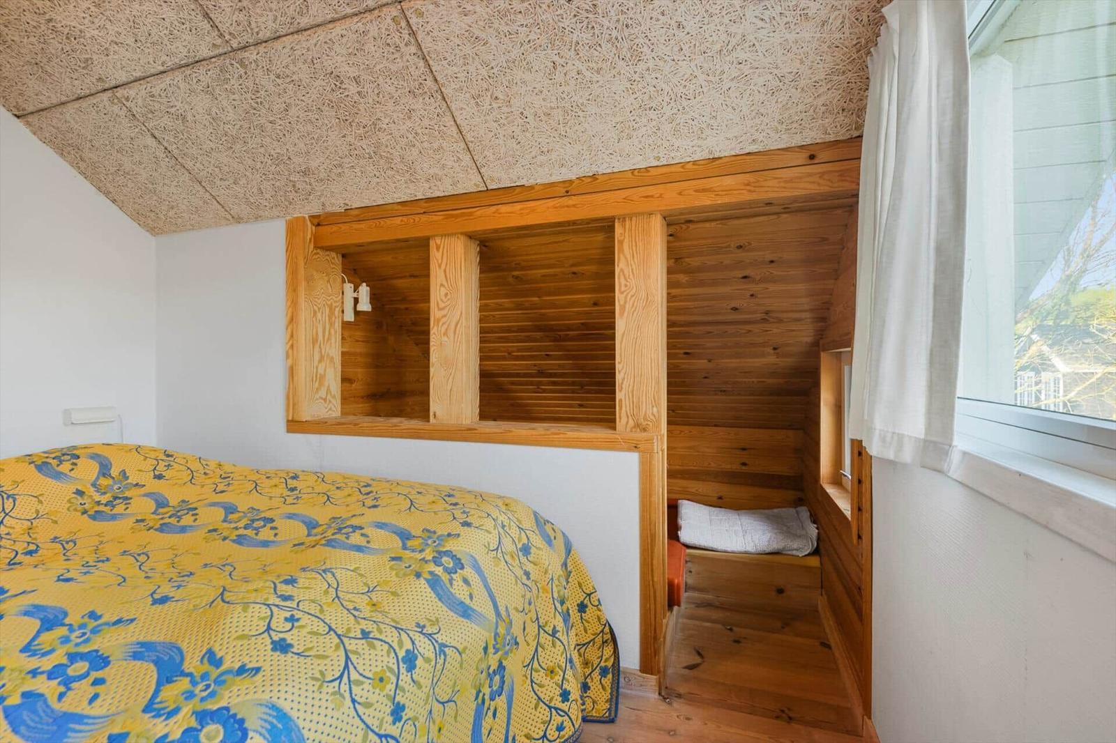 Schlafzimmer mit Holzbett und Fenster. Decke aus Holzspanplatten.