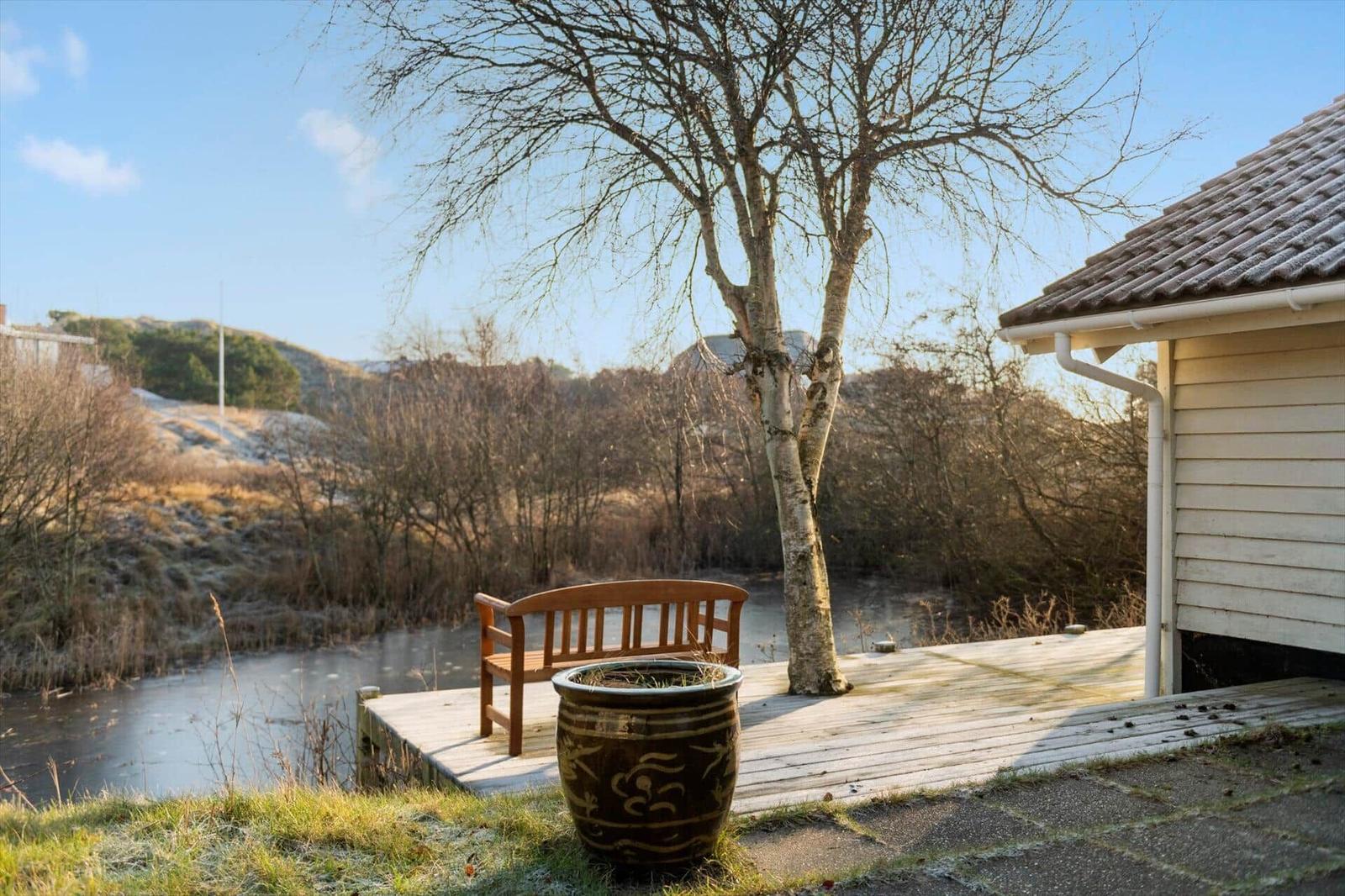 Terrasse mit Holzbank und Baum neben Haus, Blick auf Fluss und Hügel.