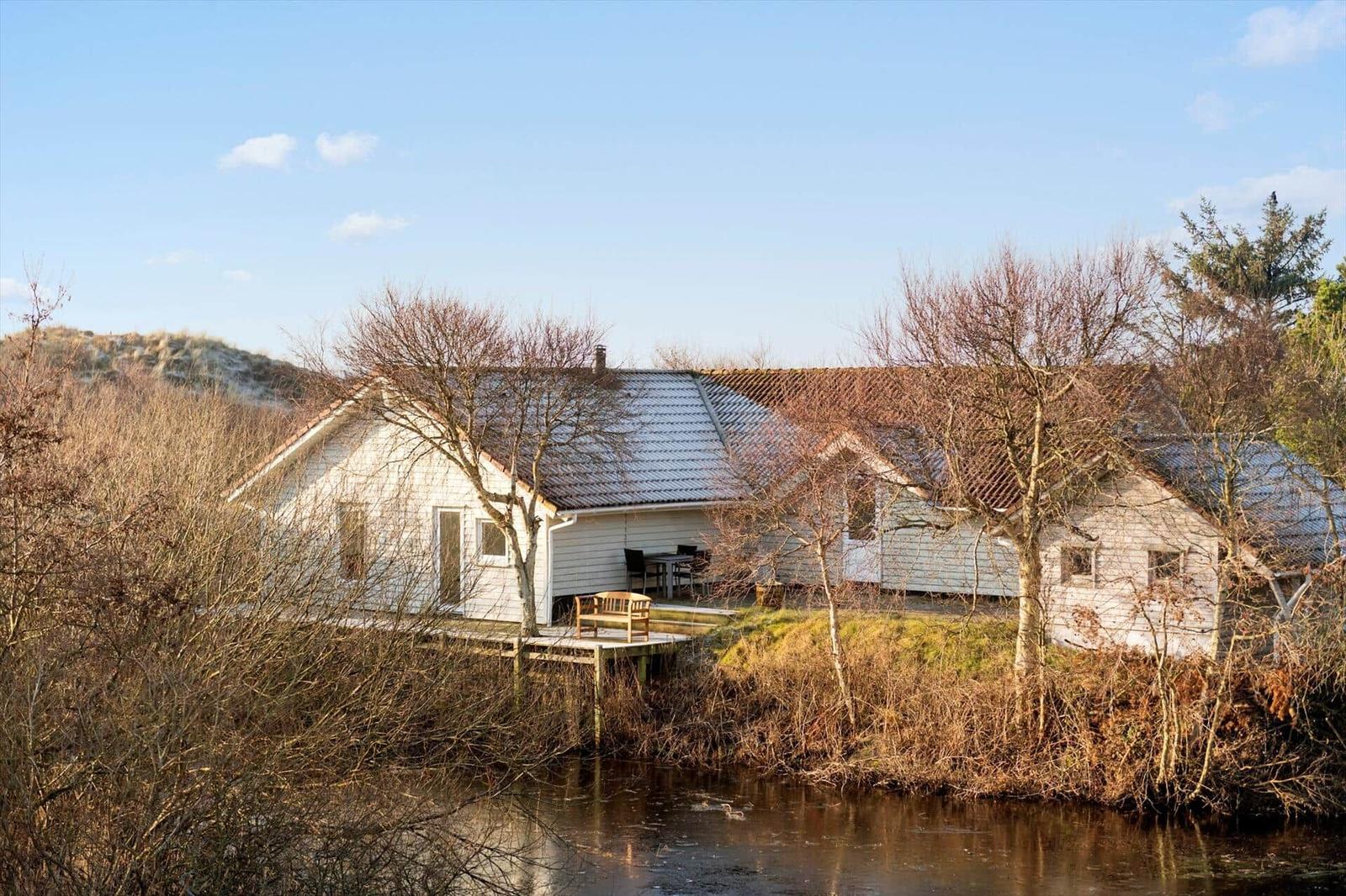 Wohnhaus mit Terrasse am Wasser, umgeben von Bäumen und Dünen.