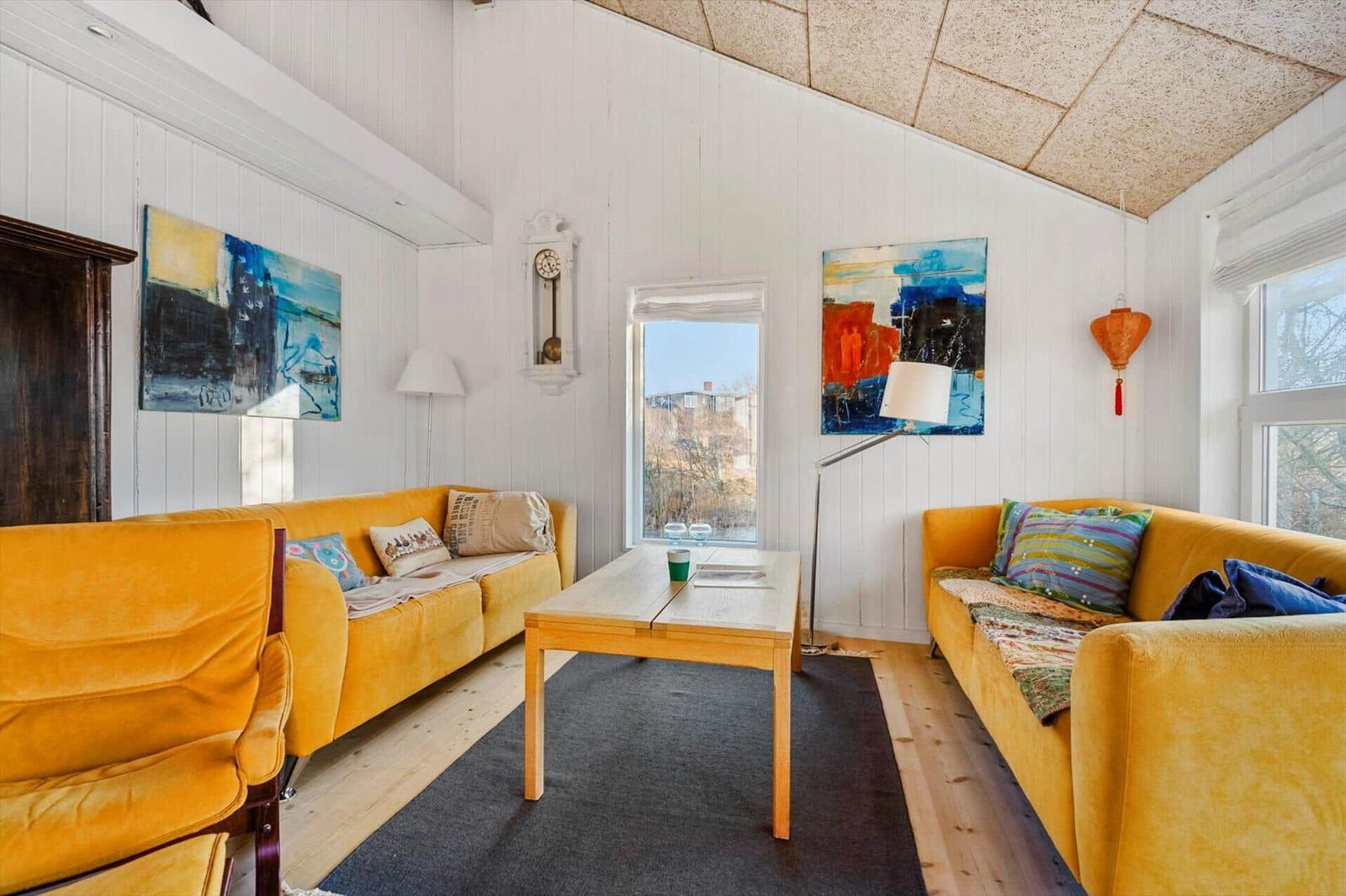 Wohnzimmer mit zwei gelben Sofas, Holztisch und Wandbildern.