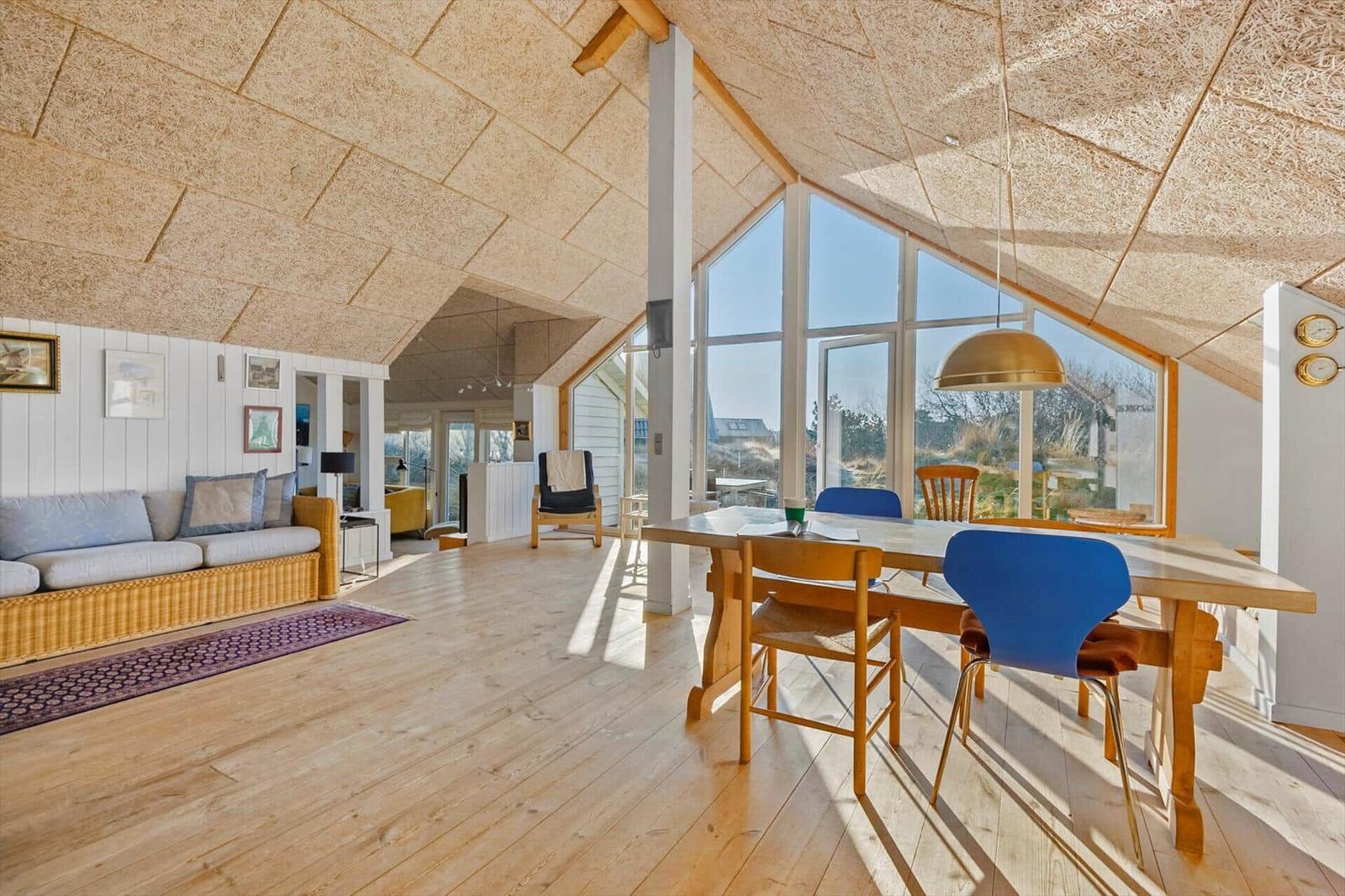 Großes Wohn- und Esszimmer mit Holzboden, großem Fenster und Holztisch mit Stühlen.