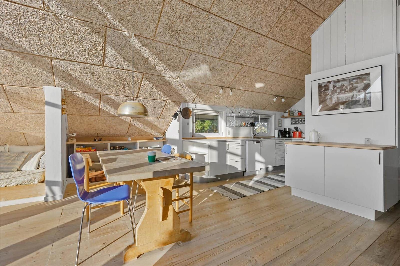 Küche mit Esstisch, Bett und Holzboden unter schrägem Dach.