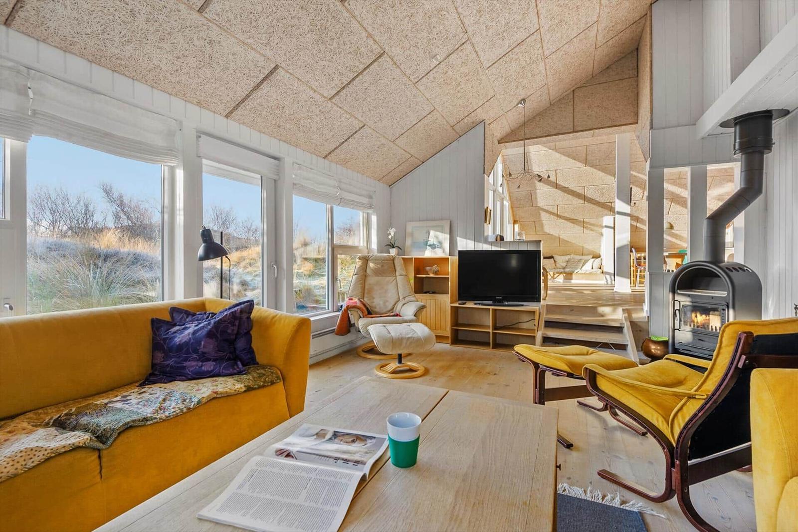 Wohnraum mit gelbem Sofa, Kamin und großen Fenstern zur Aussicht.
