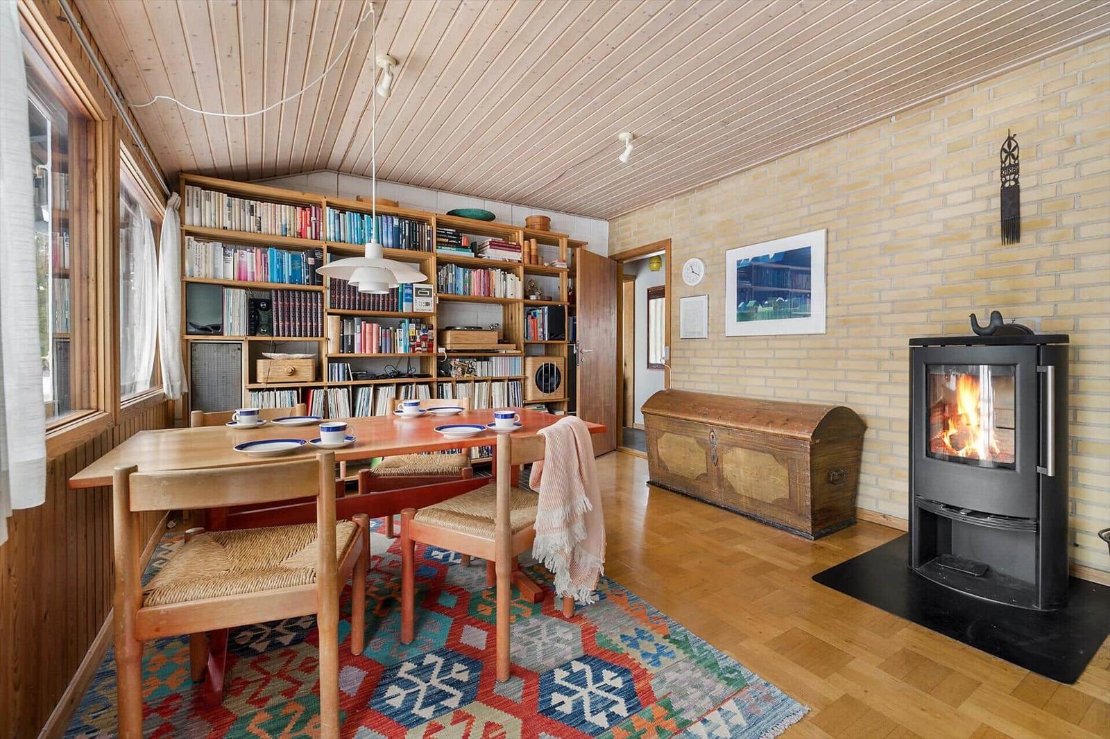 Dining room with wooden table, chairs, bookshelf, and wood stove.