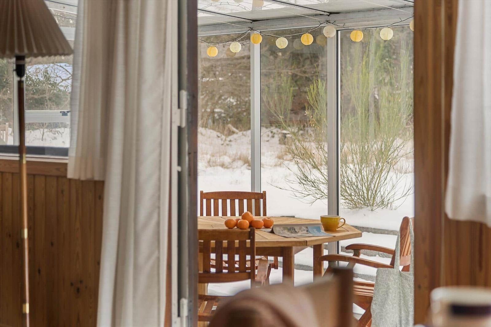 Terrace with wooden table, chairs, and snow outside. Hanging string lights and oranges on the table.