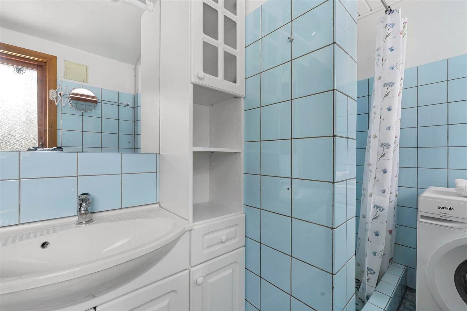 Bathroom with blue tiles, sink, mirror cabinet, and shower with curtain.