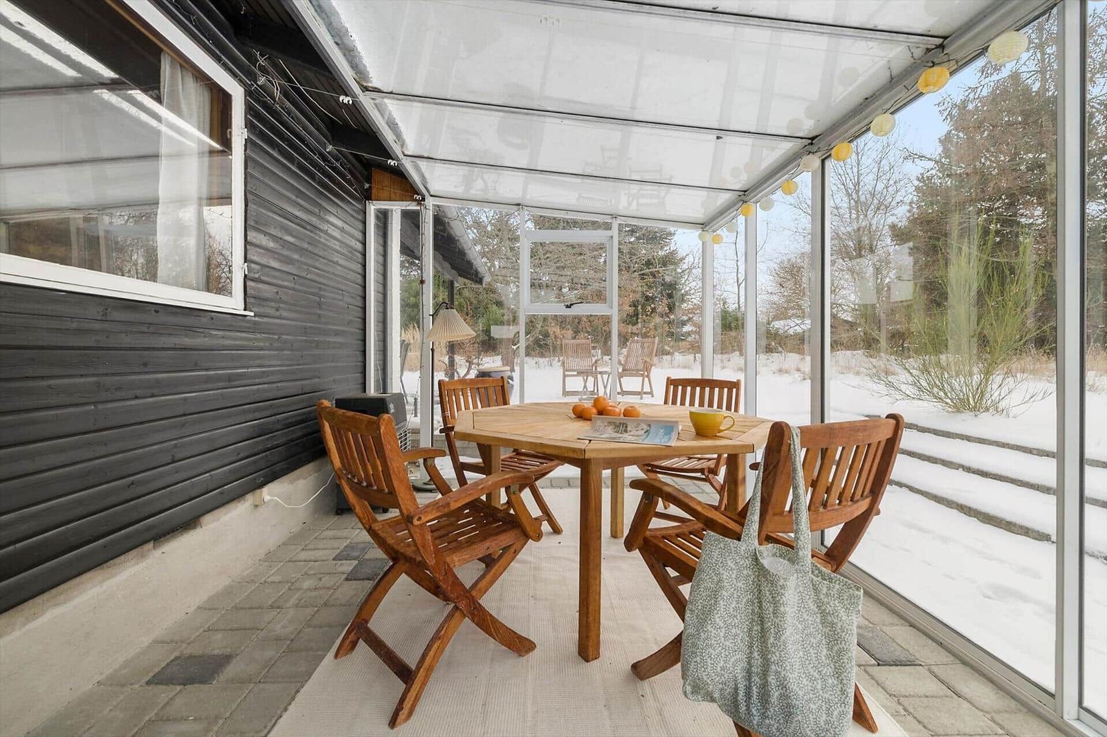 Patio with wooden table and chairs, snow outside, string lights on the ceiling.