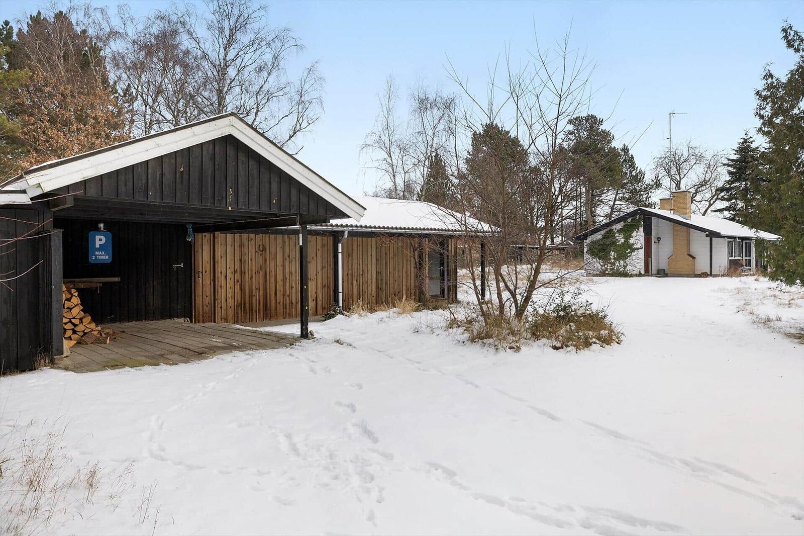 Snow-covered garden with wooden garage and holiday house in the woods.