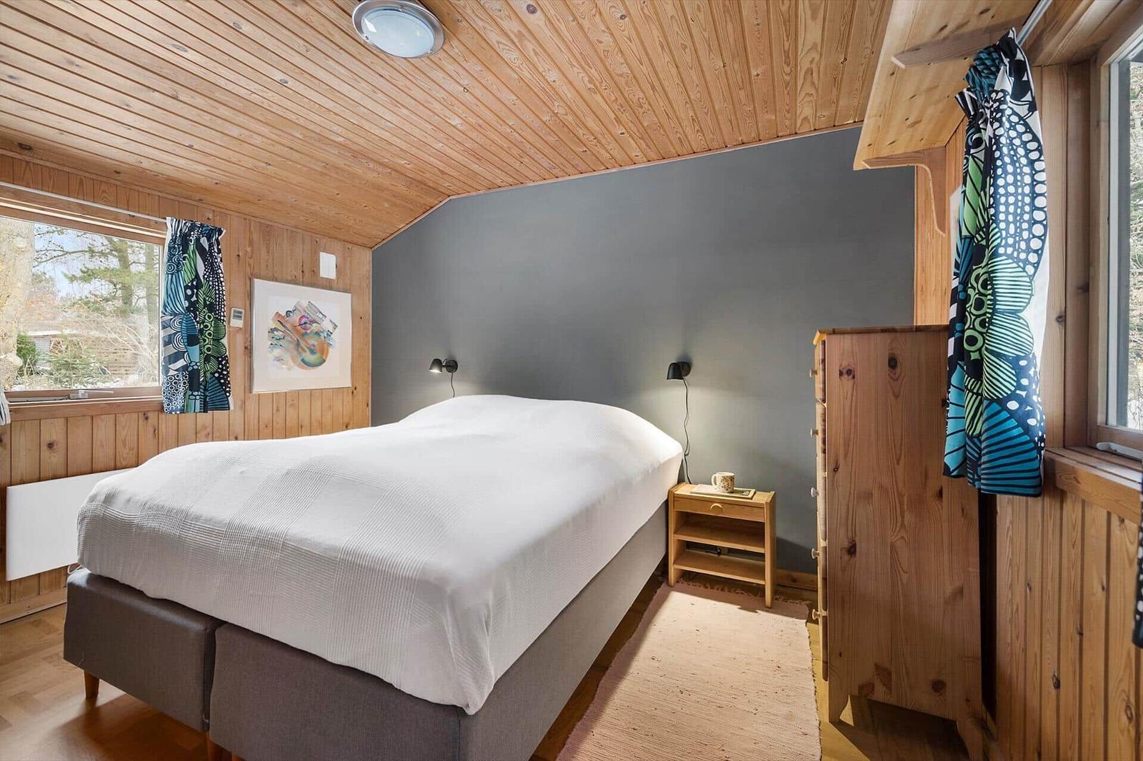 Bedroom with wooden walls, bed, nightstand, and windows.