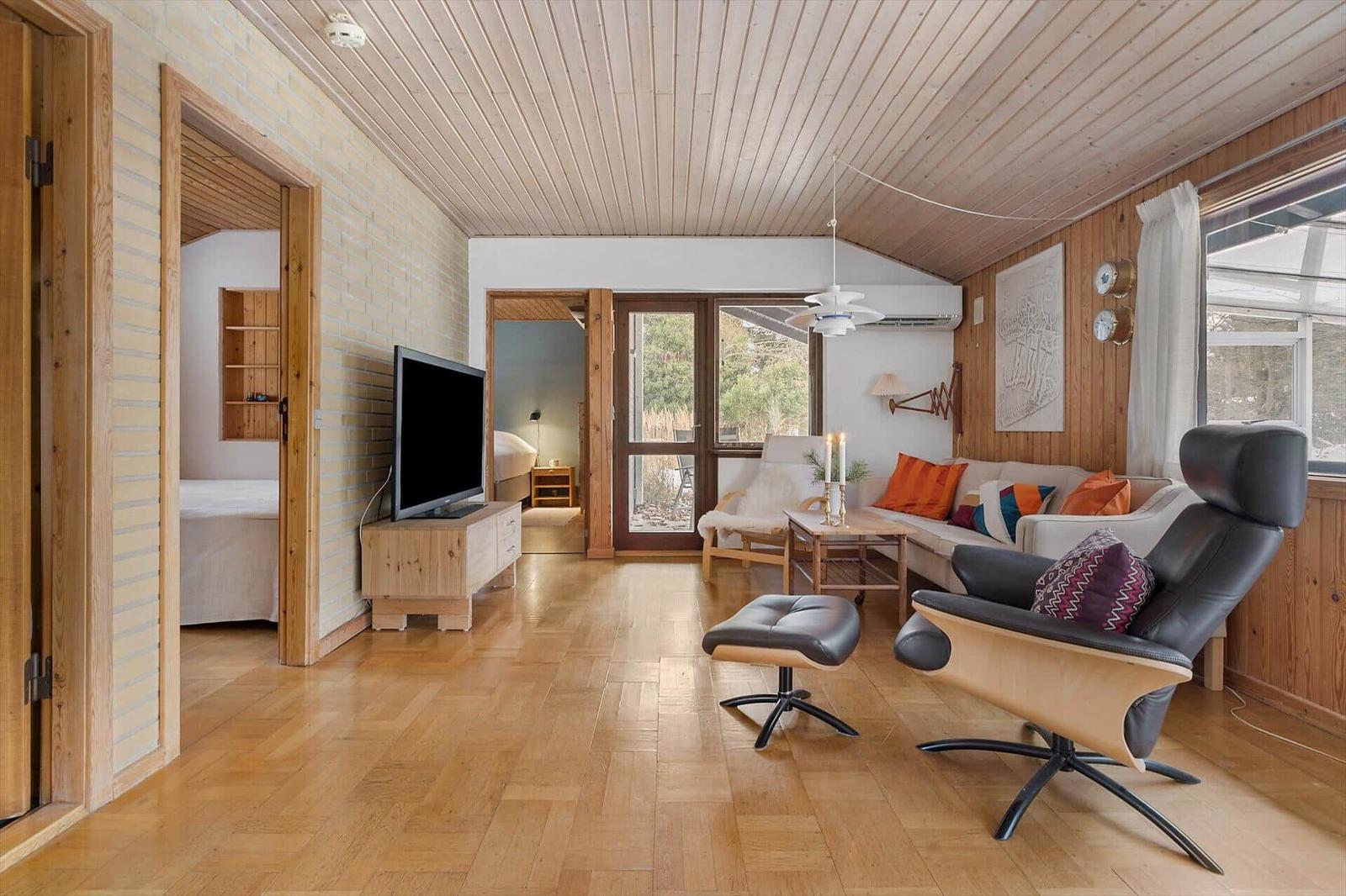 Living room with sofa, chair, and TV. Wooden ceiling and floor. Doors to bedroom and terrace.