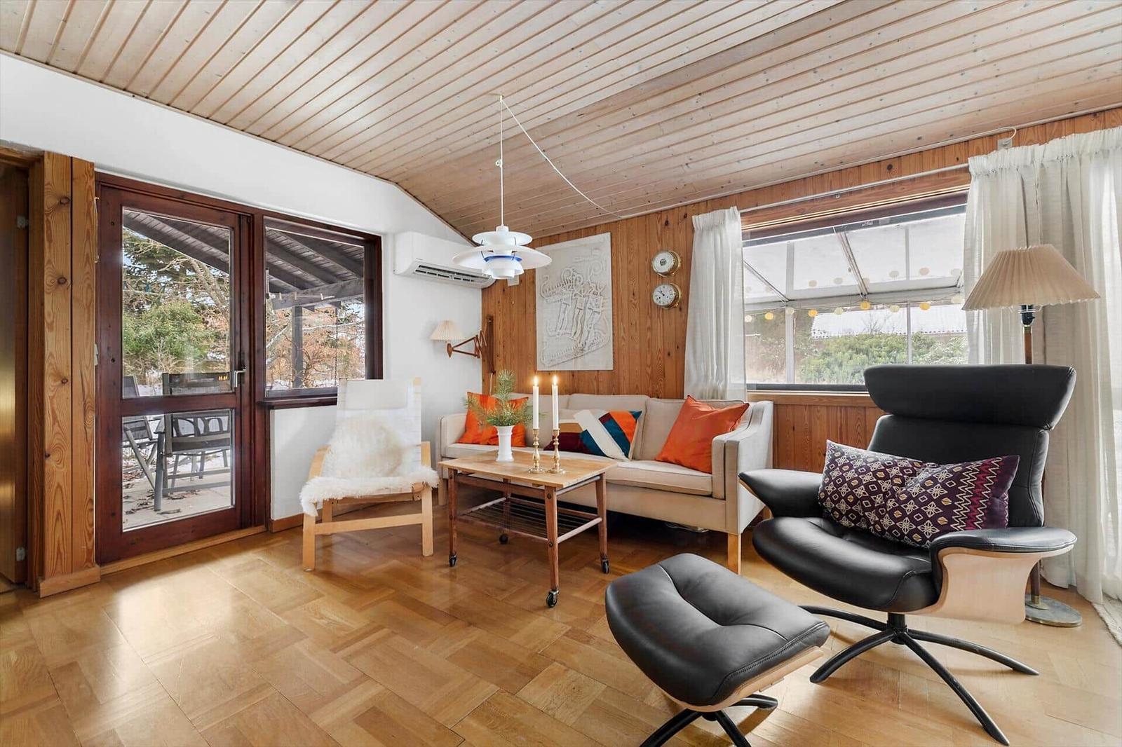 Living room with wooden ceiling, sofa, armchair, and terrace door.