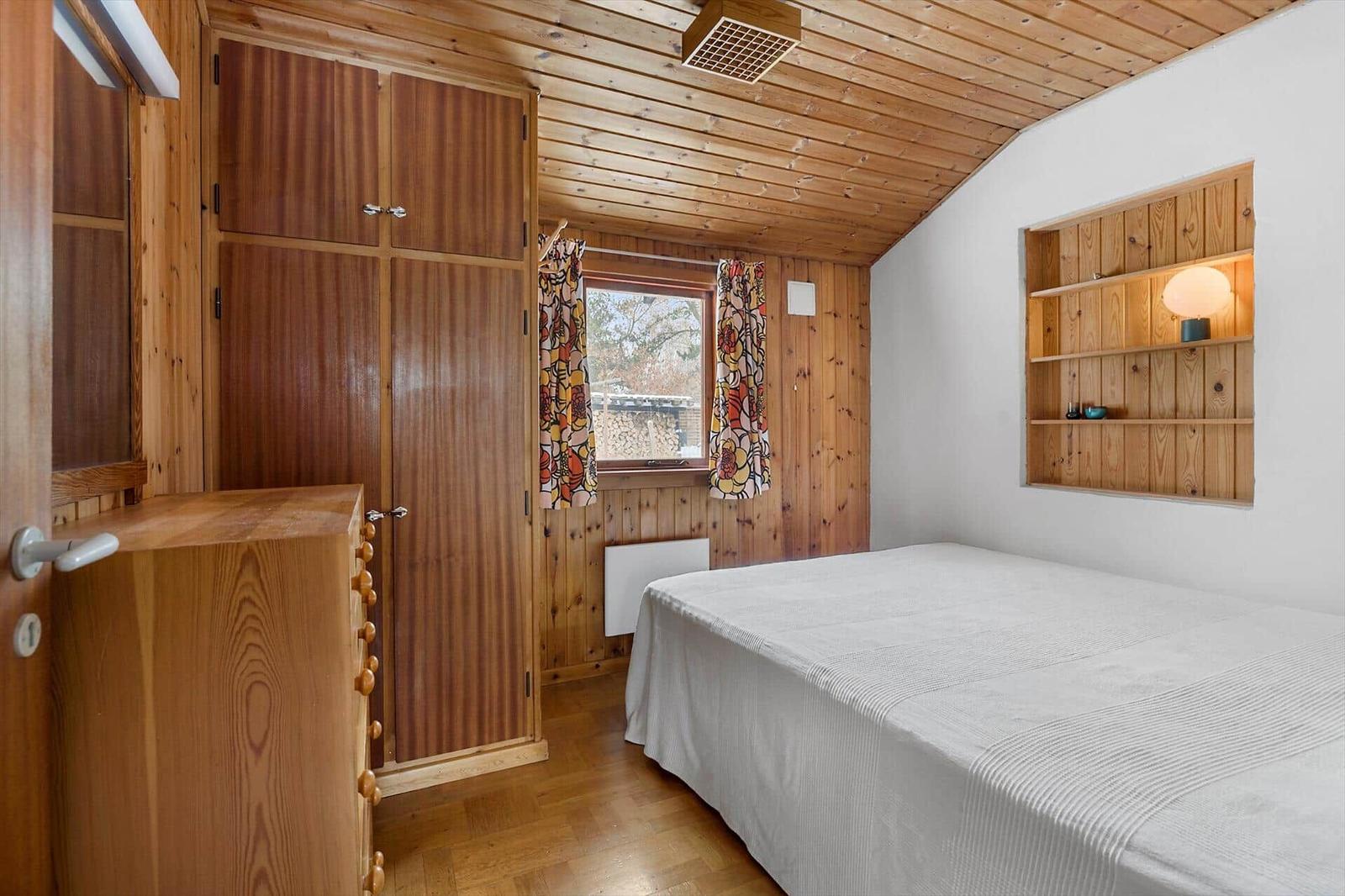 Bedroom with wooden floor, bed, wardrobe, and window with curtains.
