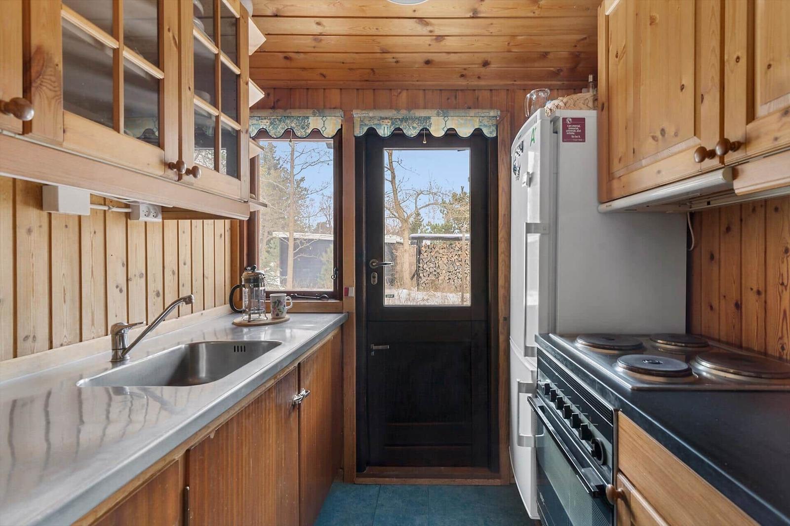 Kitchen with wood walls, refrigerator, stove, and window to outside door.