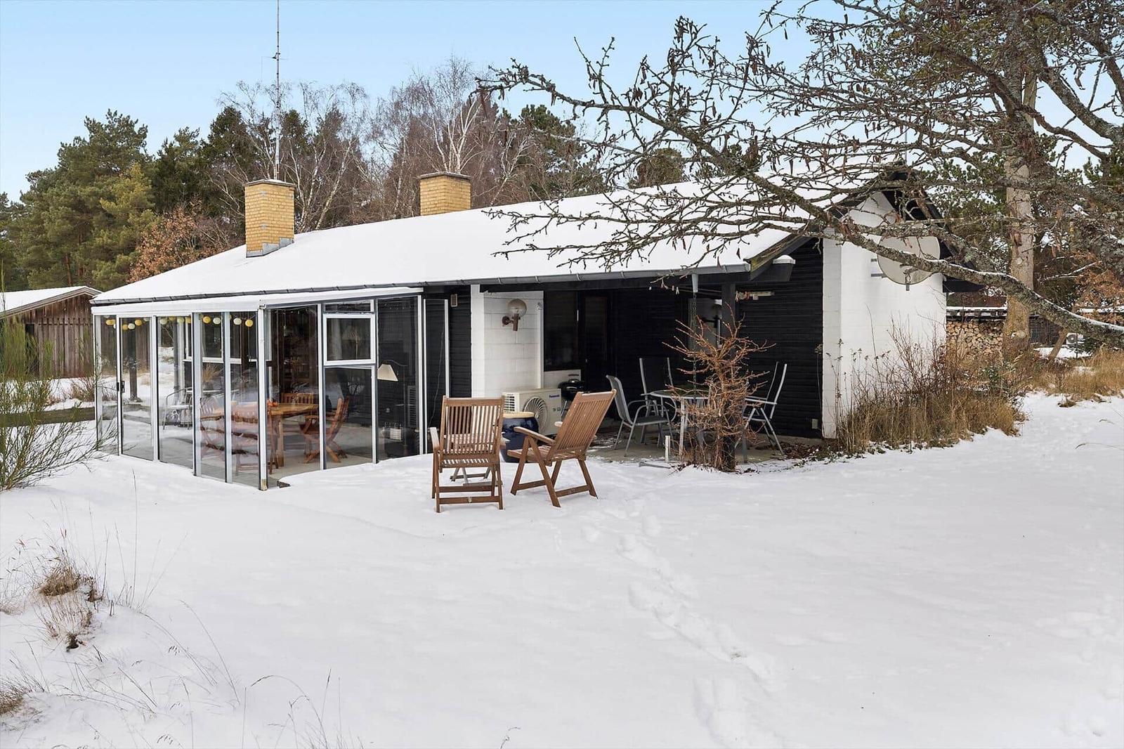 House with snow-covered roof, terrace, and garden furniture in winter.