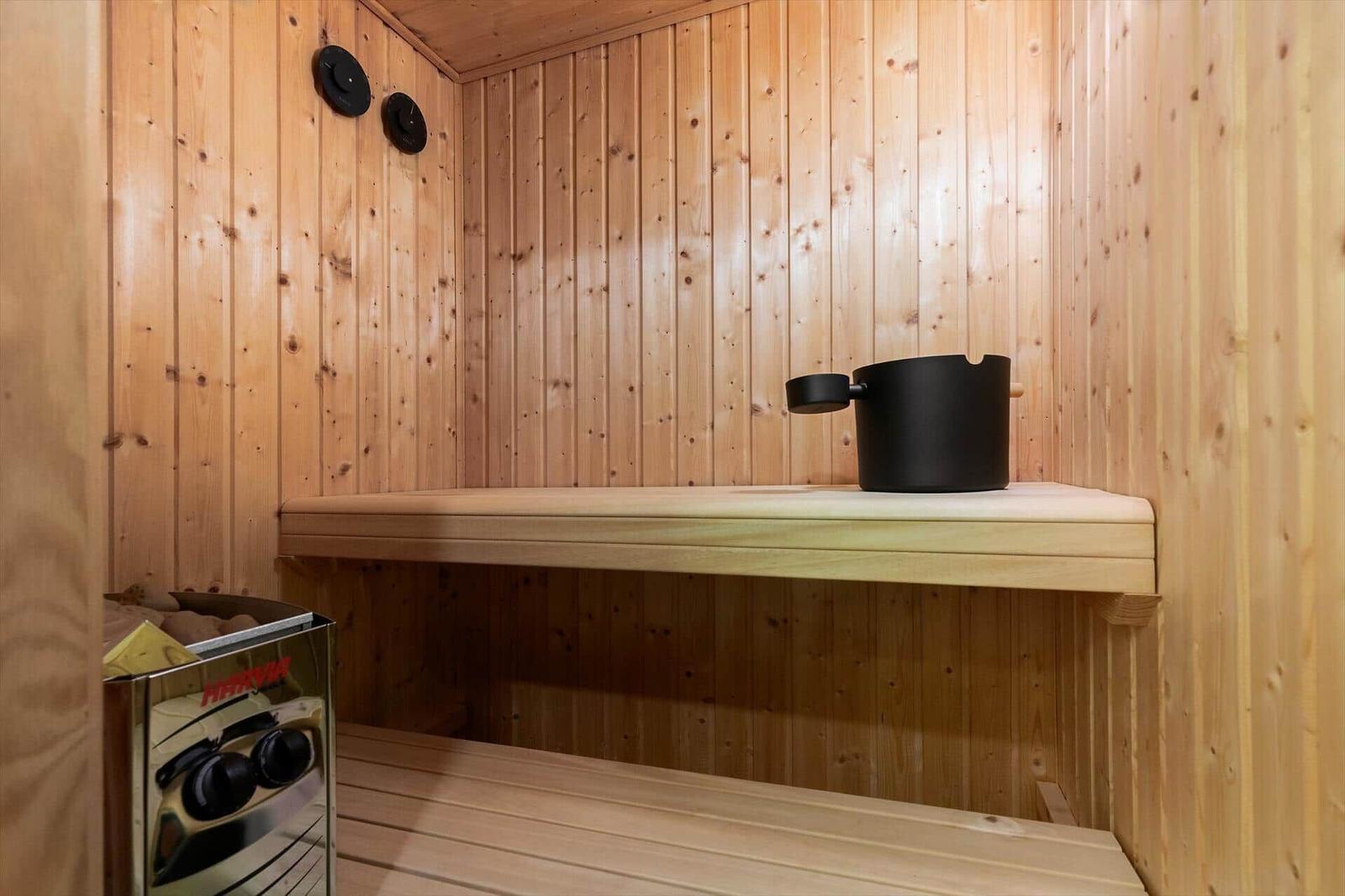 Sauna with wooden walls, bench, and black bucket.