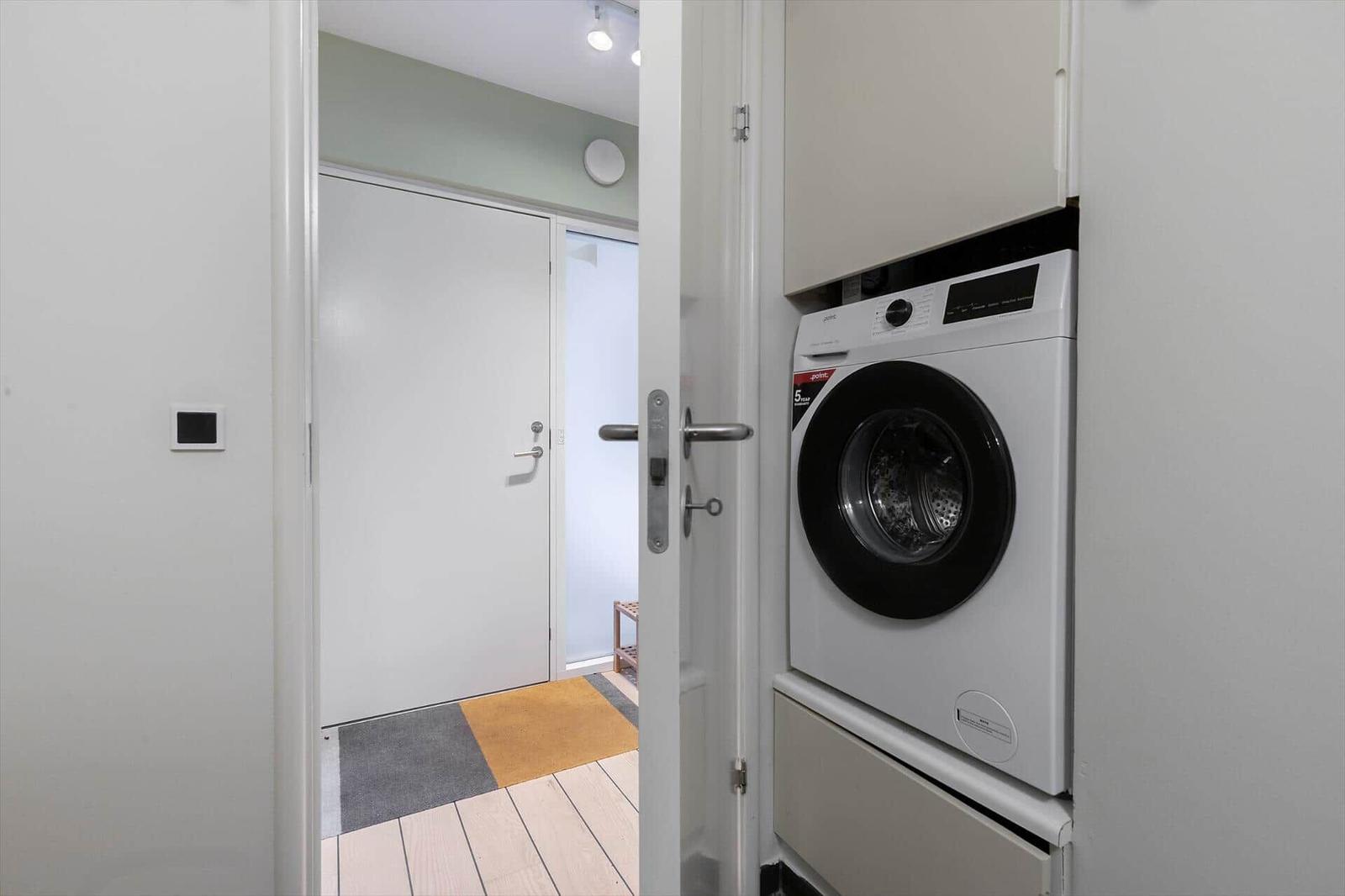 Washing machine in a narrow room next to a door with tiled floor.