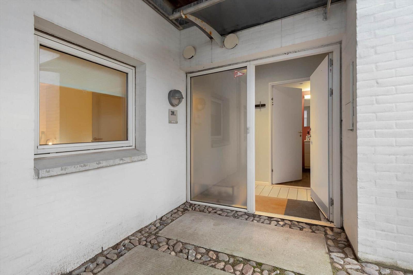 Entrance with glass door and window. White walls and stone path.