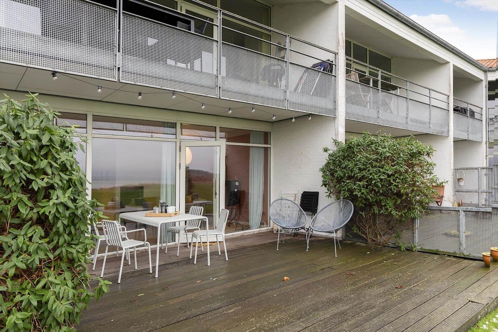 Deck with table, chairs, and chairs. Background: balcony with mesh and windows.