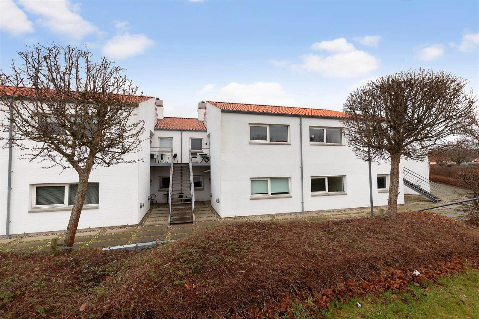 White vacation apartment with red roof, balcony, and stairs to the entrance door.