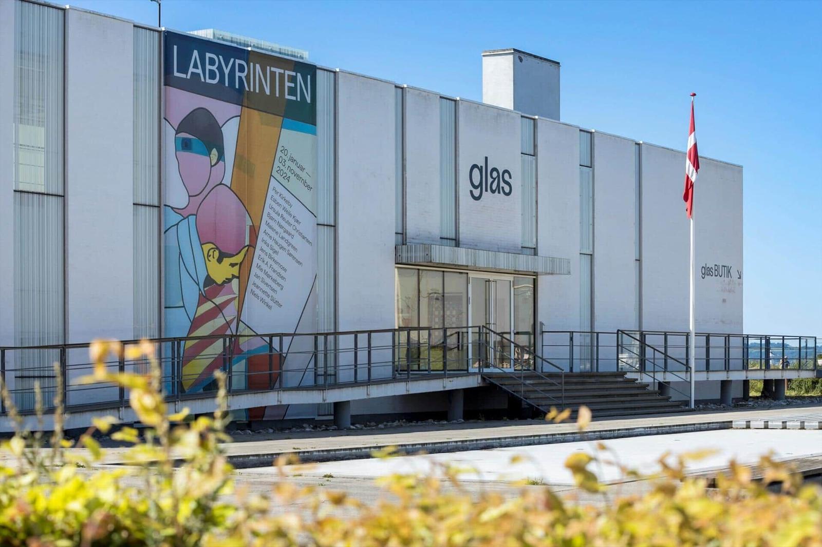 Modern glass gallery with large wall art and flag. Entrance with stairs and railing.