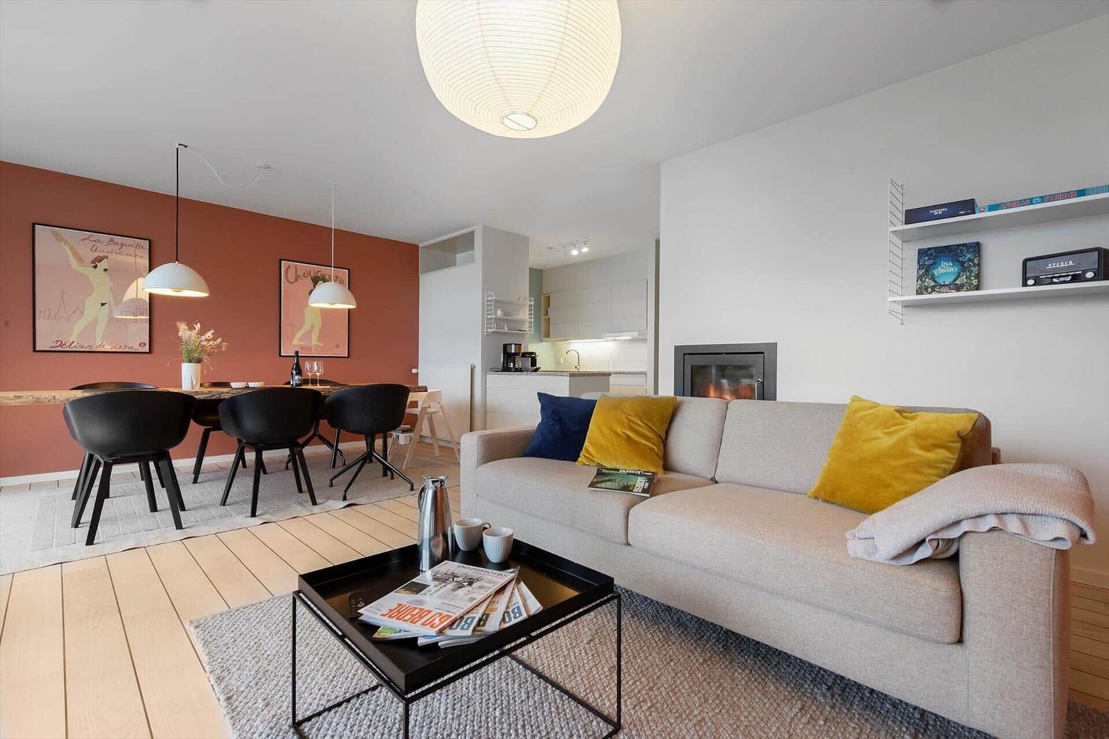 Living room with sofa, coffee table, and fireplace. Dining area with table and chairs. Kitchen area visible.