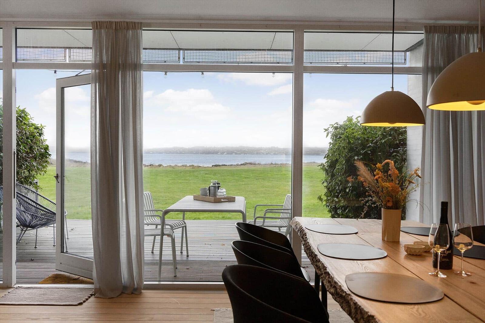 Dining room with view of lawn and water. Table, chairs, and pendant lamp visible.