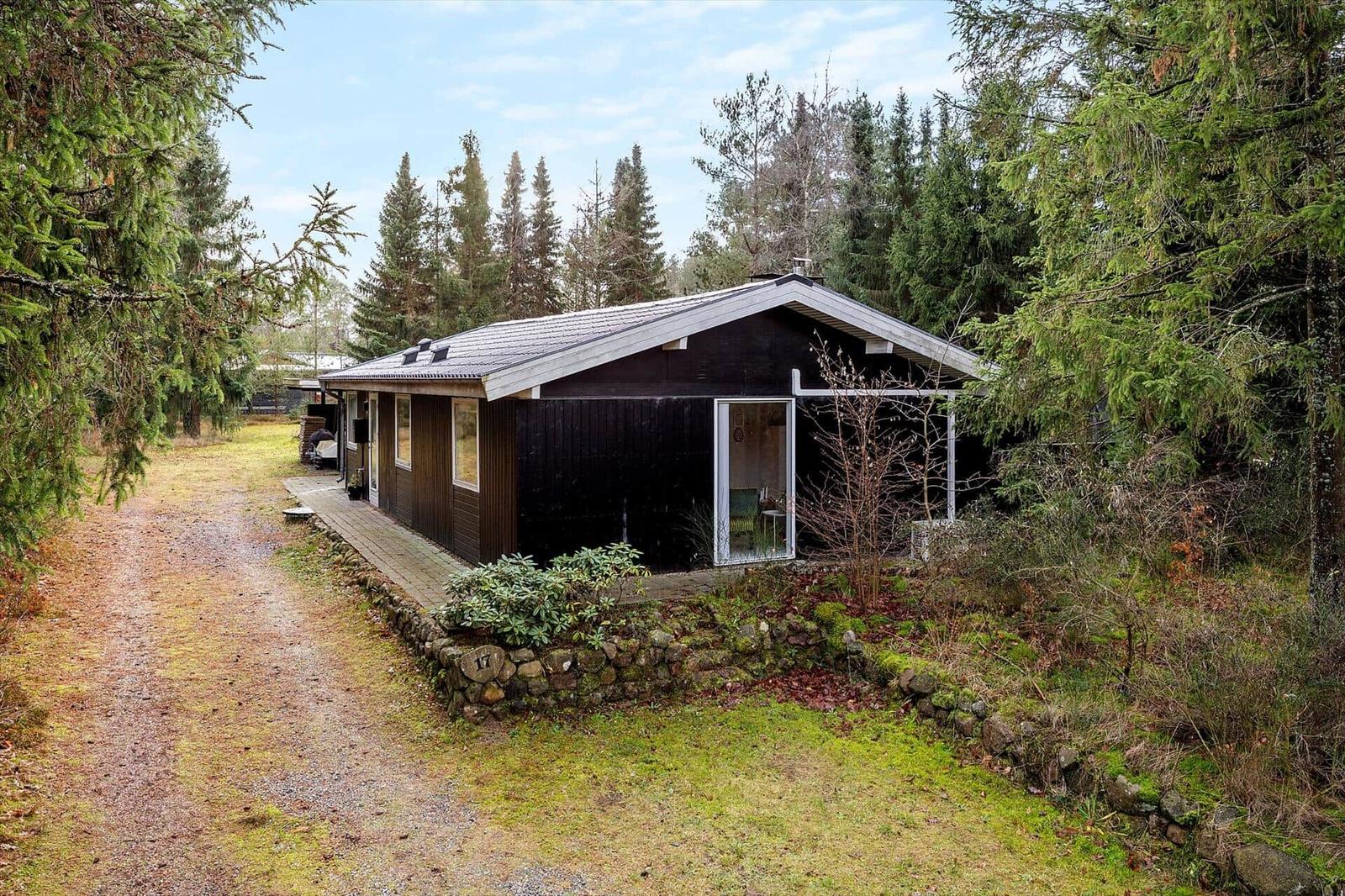A dark wooden house with glass front and stone wall in the forest.