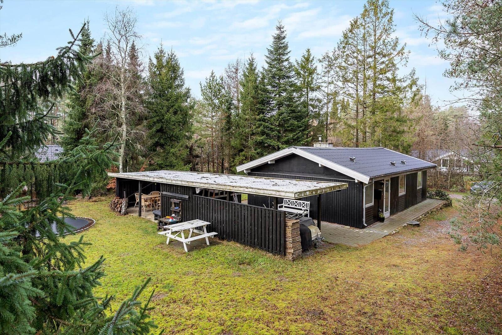 Wooden house with terrace, grill, and picnic table in the forest.