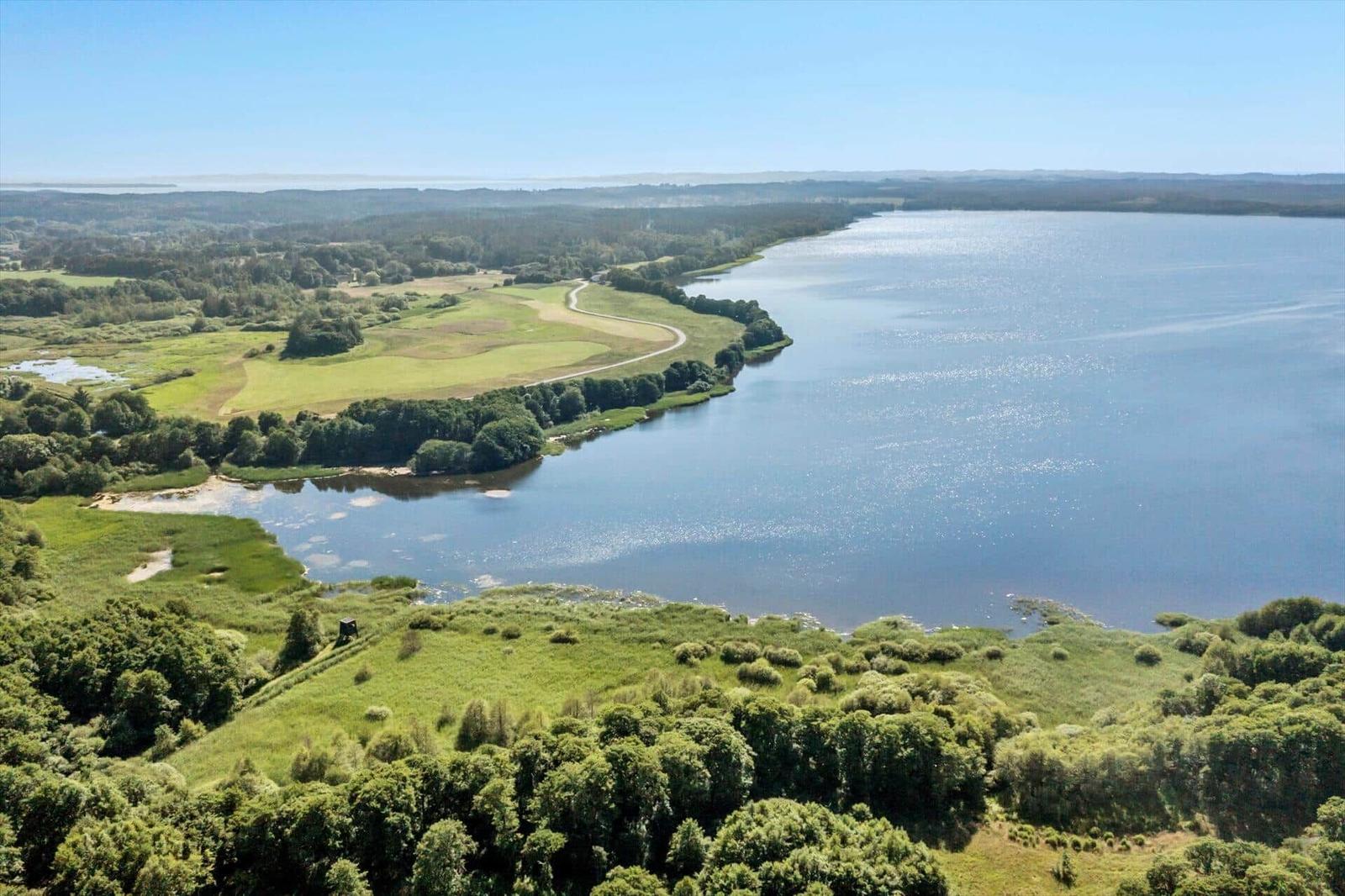 Large lake with green shorelines and forested areas under a blue sky.