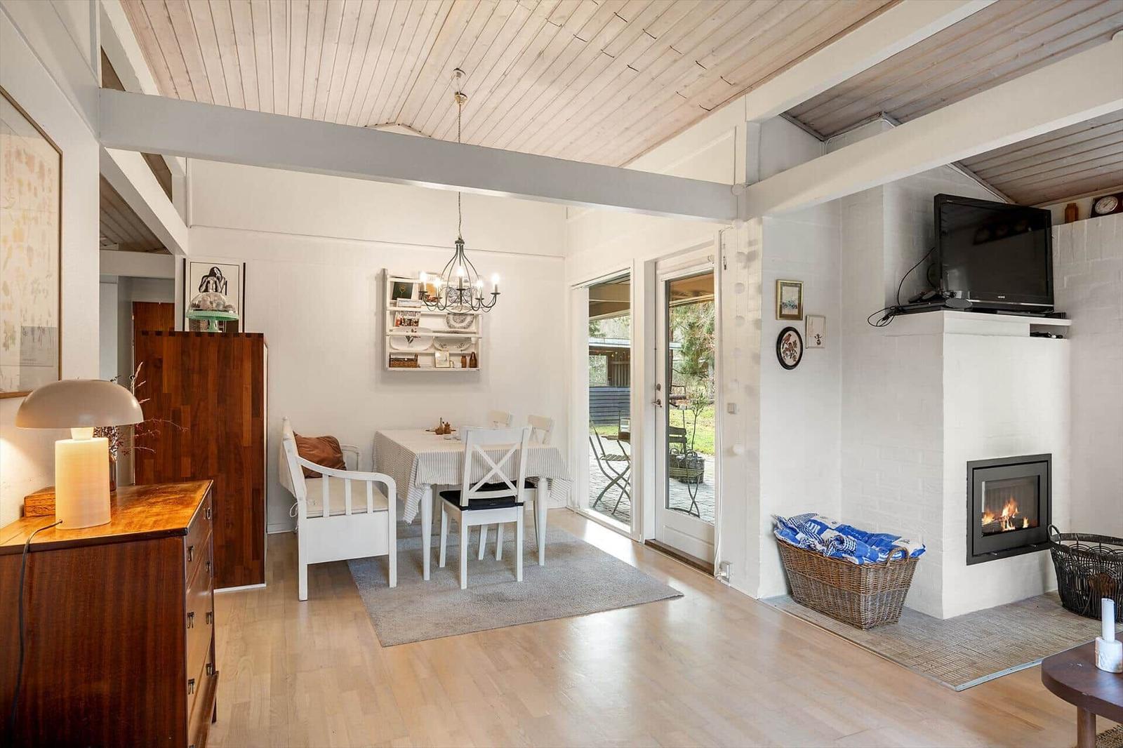 Living and dining area with fireplace, table and chairs, wooden floor and glass door to terrace.