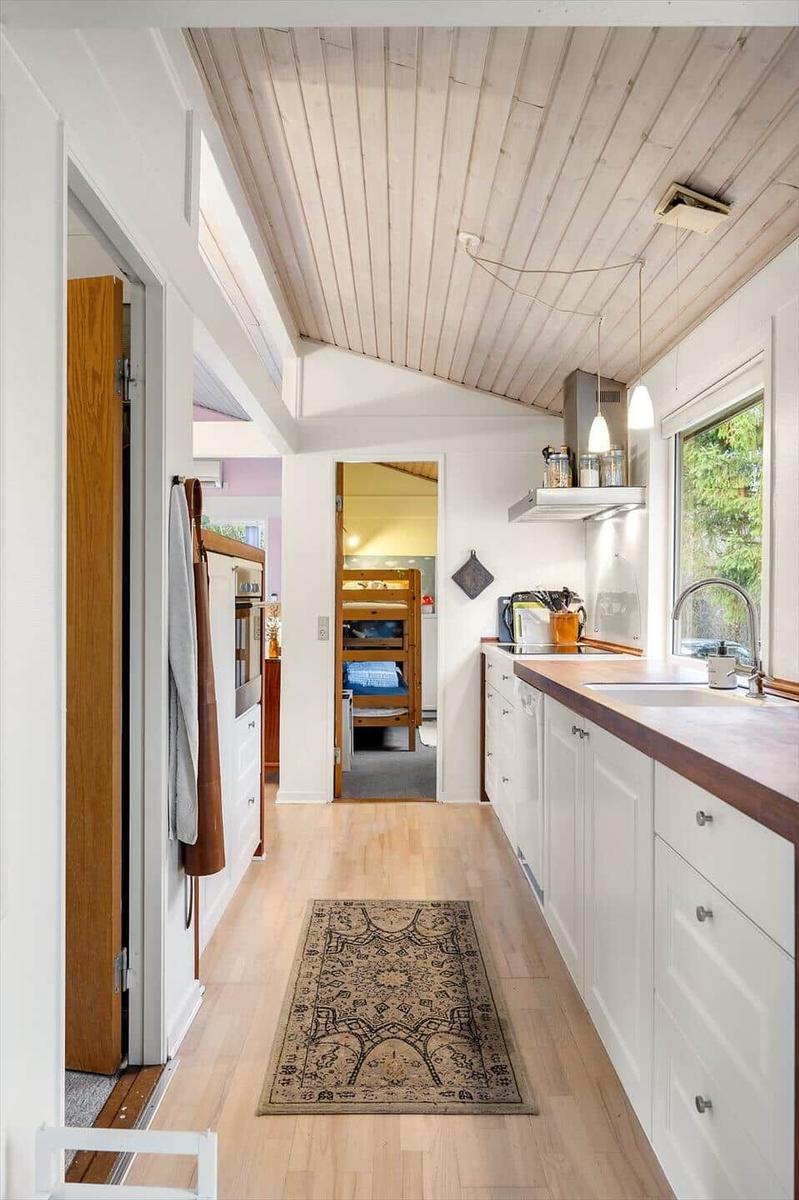 Kitchen with wooden floor, white cabinets, and view into bedroom with bunk bed.
