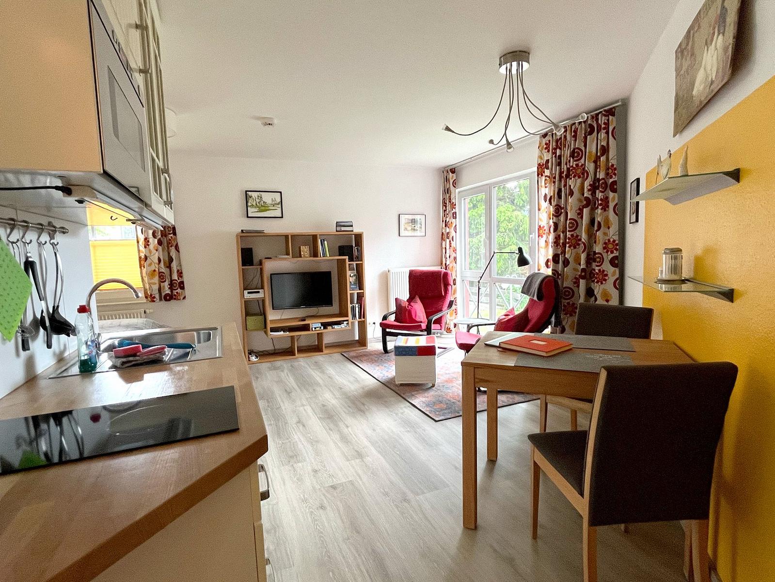 Küche, Essbereich und Wohnzimmer mit TV, Sitzgelegenheiten und Balkonzugang.