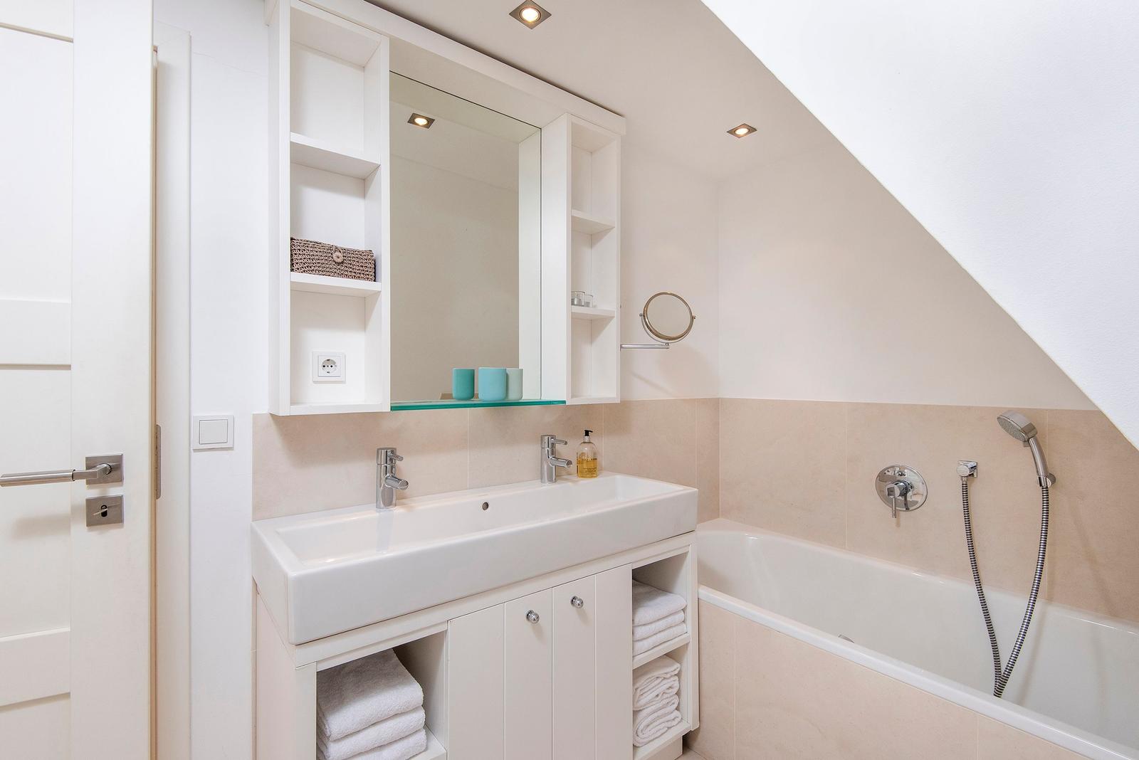 Badezimmer mit Waschbecken, Spiegelschrank und Badewanne unter Dachschrägen.