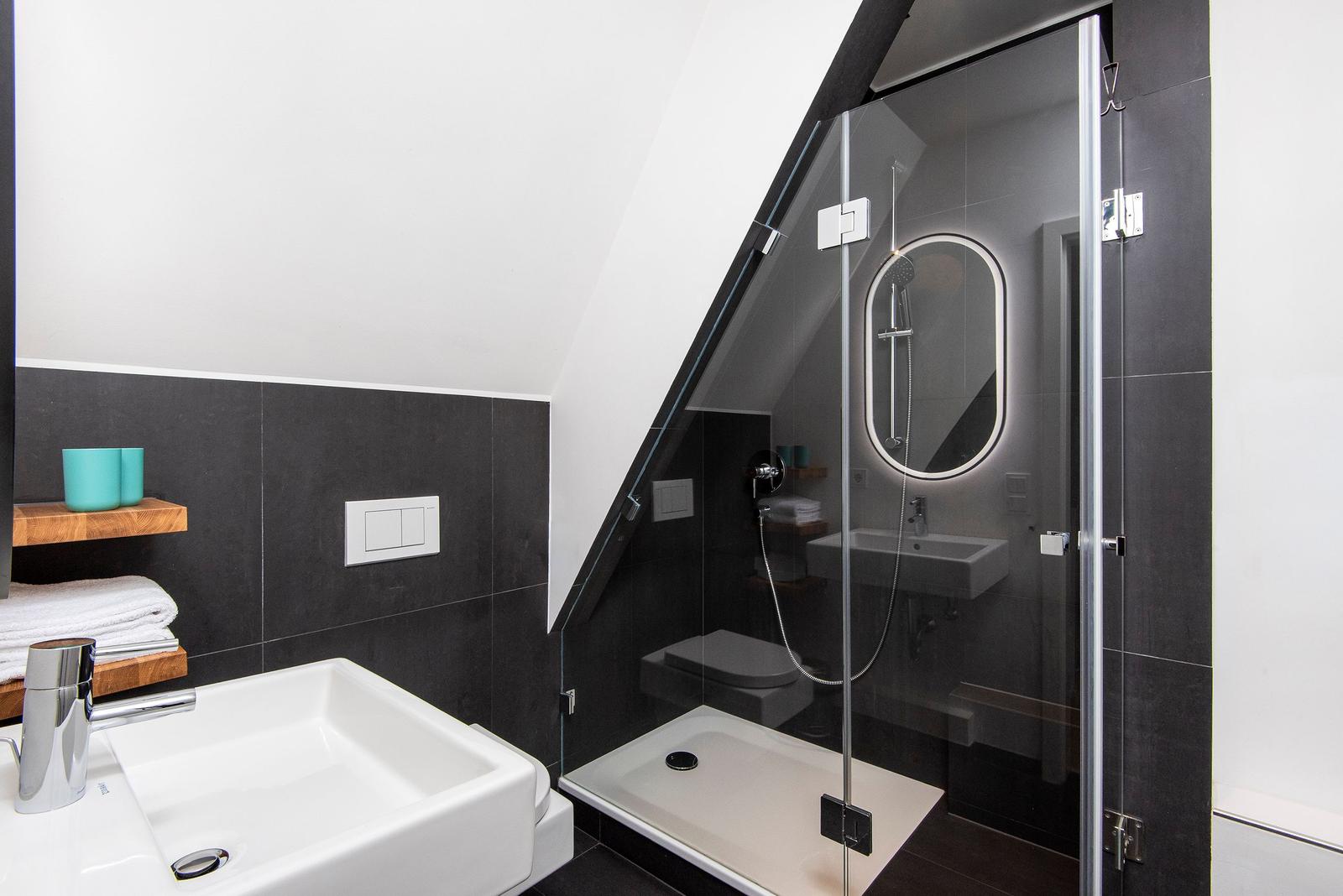 Dusche mit Glaswand, Waschbecken und Toilette unter Dachschrägen