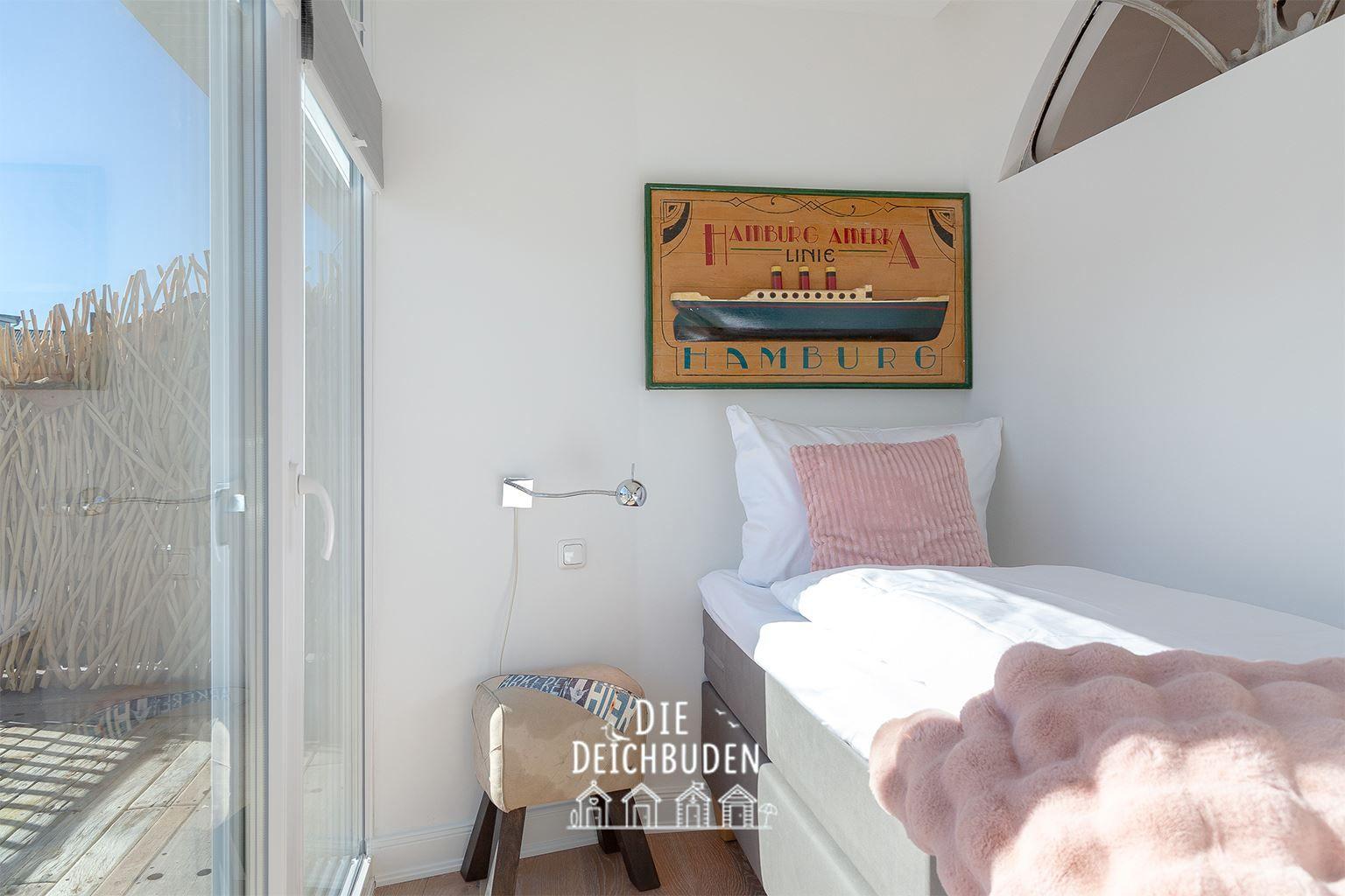 Schlafzimmer mit Bett, Kissen und Wandbild. Durchgang zur Terrasse mit Holzgeländer.