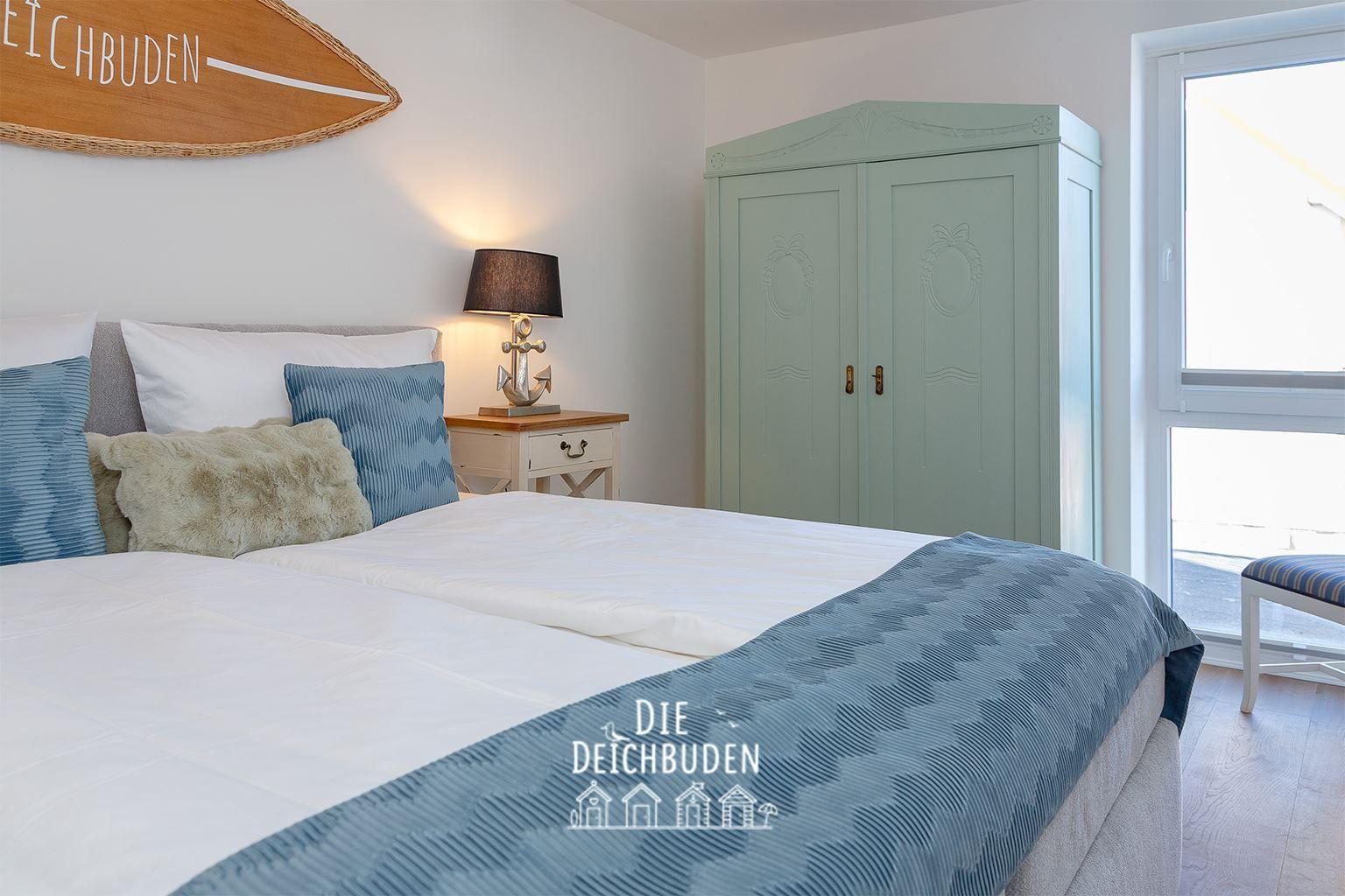 Schlafzimmer mit Bett, Kleiderschrank und Fenster. Wanddekoration und Nachttisch sind sichtbar.