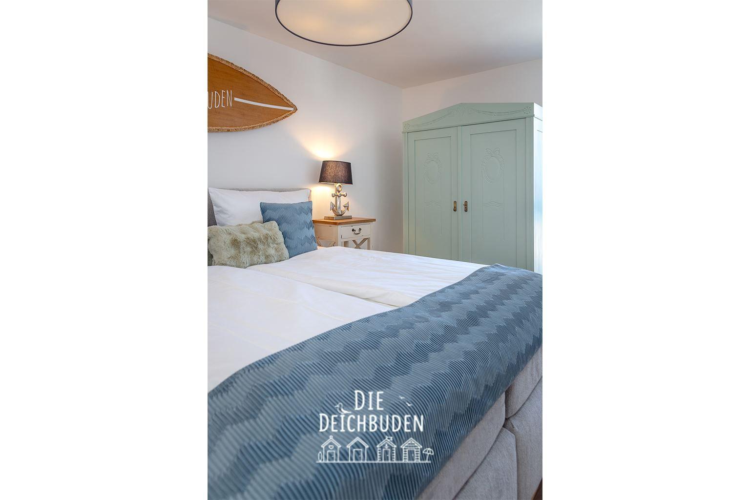 Schlafzimmer mit Bett, Nachttisch und Kleiderschrank. Wanddekoration mit Surfbrett.