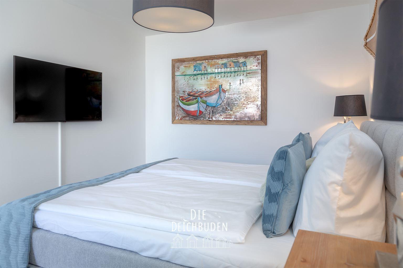 Schlafzimmer mit Bett, Wandbild und Fernseher.