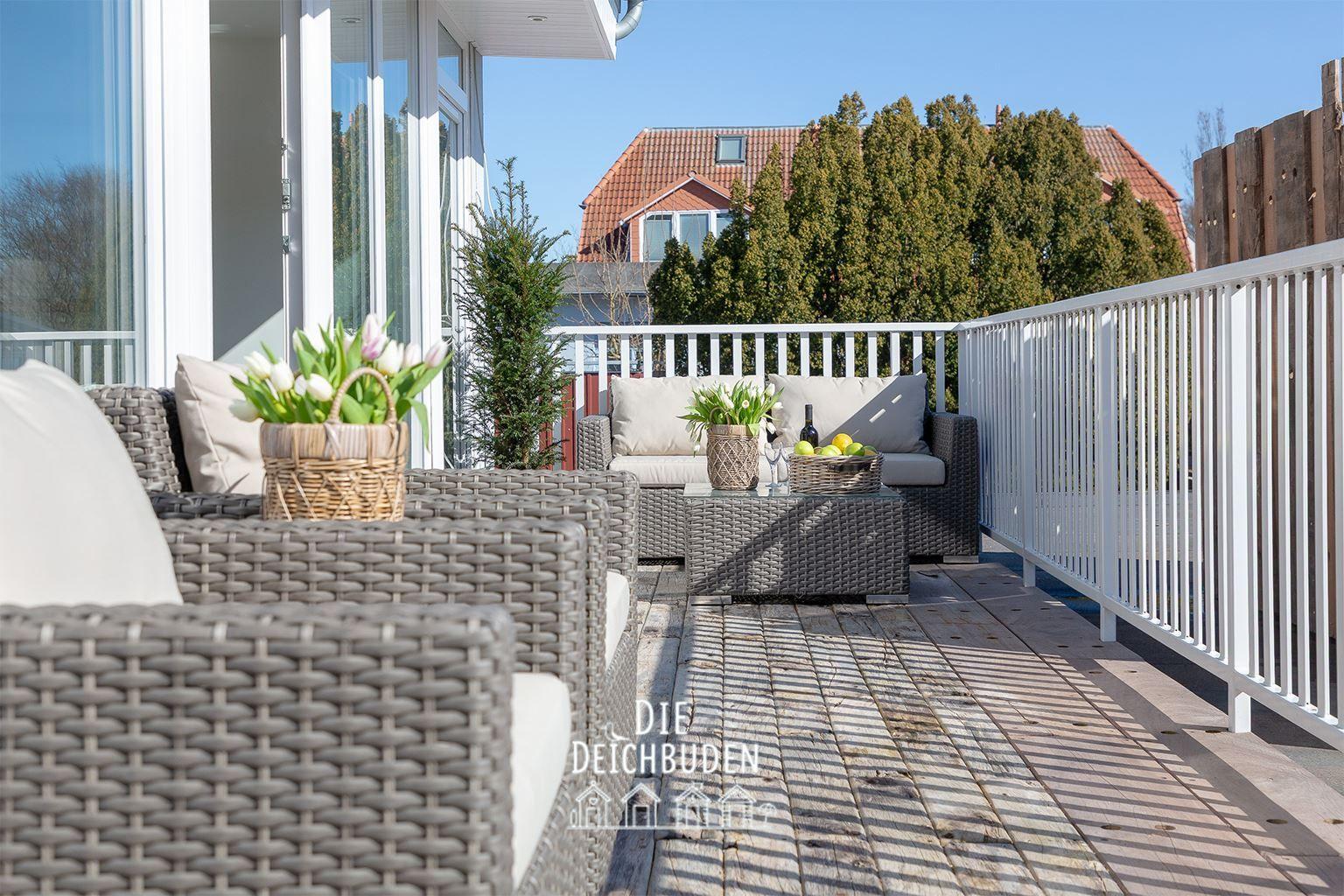 Terrasse mit Rattanmöbeln, Blumen und Blick auf Haus und Bäume.