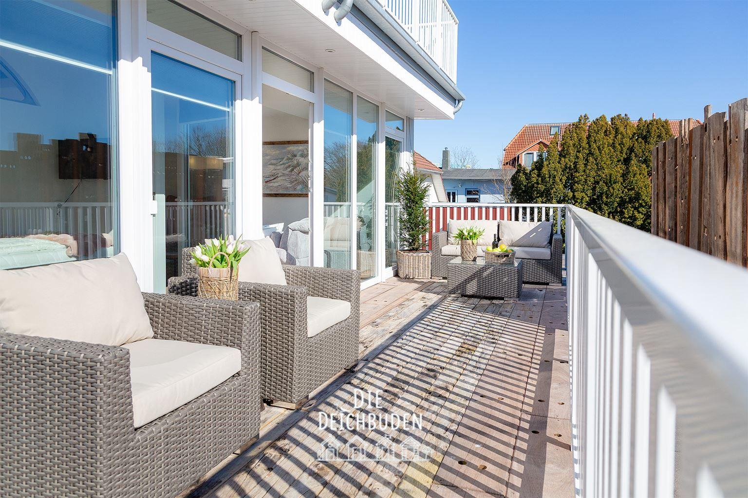 Terrasse mit Rattanmöbeln, Blumen und Blick auf Wohnbereich.